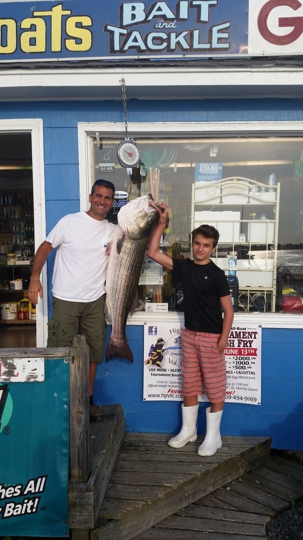Two people outside a bait shop holding a large fish, with a blue storefront behind them.