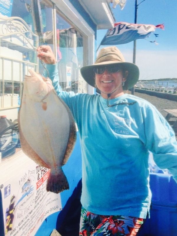 Person holding a large fish on a sunny boat deck, wearing a blue shirt and wide-brimmed hat.