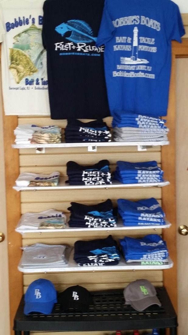 Shelved display of T-shirts and caps in navy, blue, white, and gray, likely souvenir apparel in a shop.