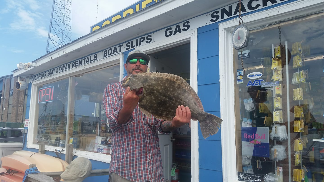 Man holding a large fish outside a gas station snack shop in winter snow