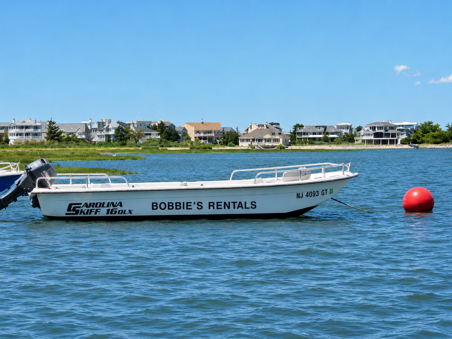 White speedboat on choppy blue water near a red buoy, with houses along the distant shore.