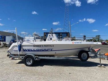 White speedboat on trailer at a boatyard under a blue sky, with rental text on the hull