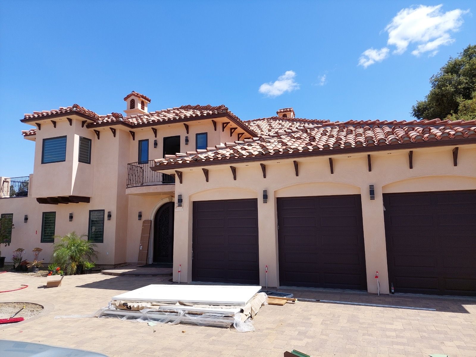 Mediterranean-style house with red tile roof, stucco walls, and three garage doors under a blue sky