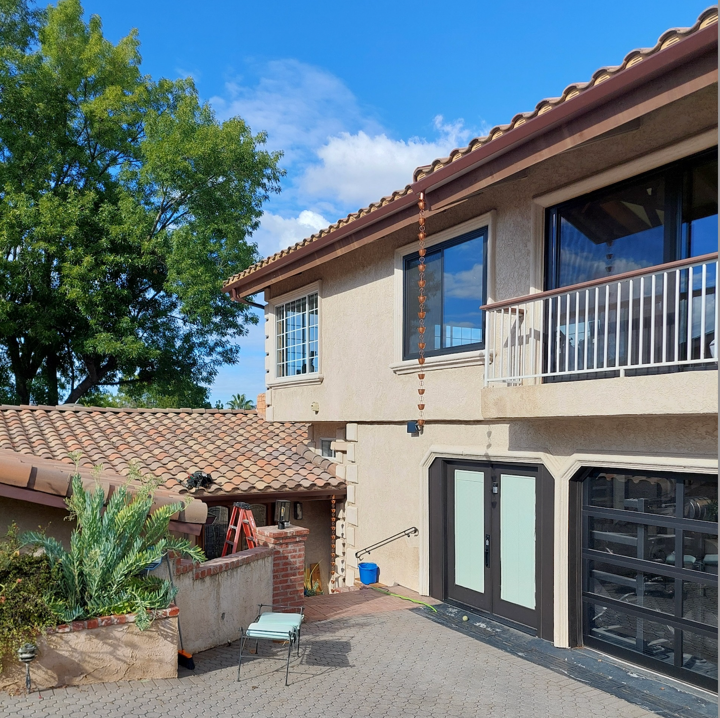 Exterior of a stucco house with balcony, garage doors, tiled roof, and a sunny courtyard