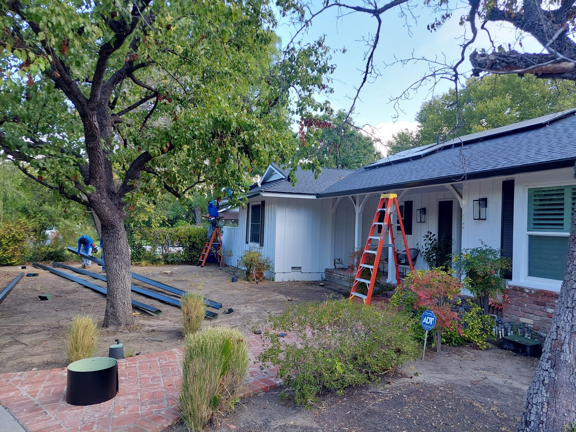 Front yard of a house with trees, landscaping, and ladders by the porch under repair.