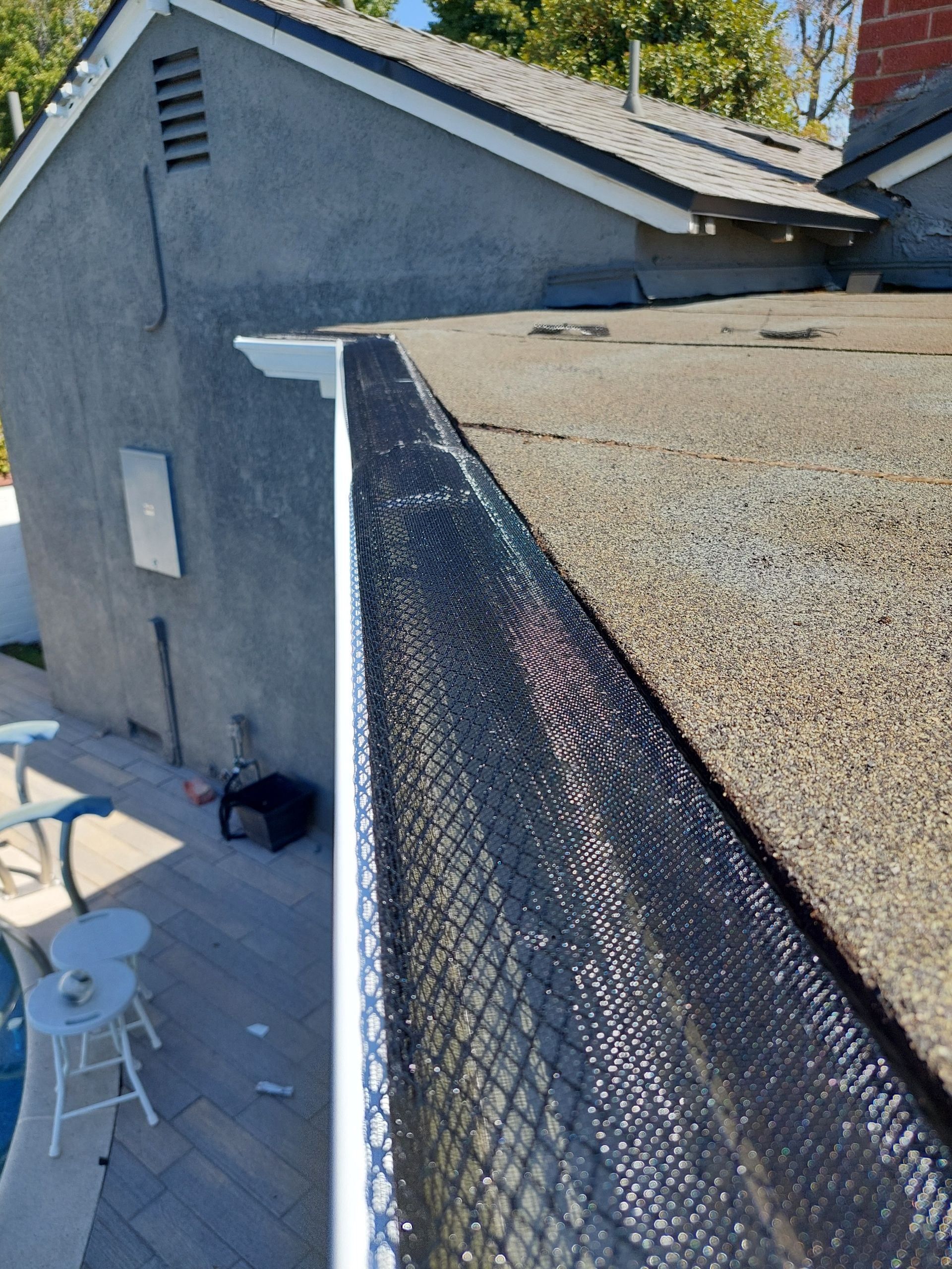 Rooftop edge with black mesh gutter guard beside a gray building under a sunny sky
