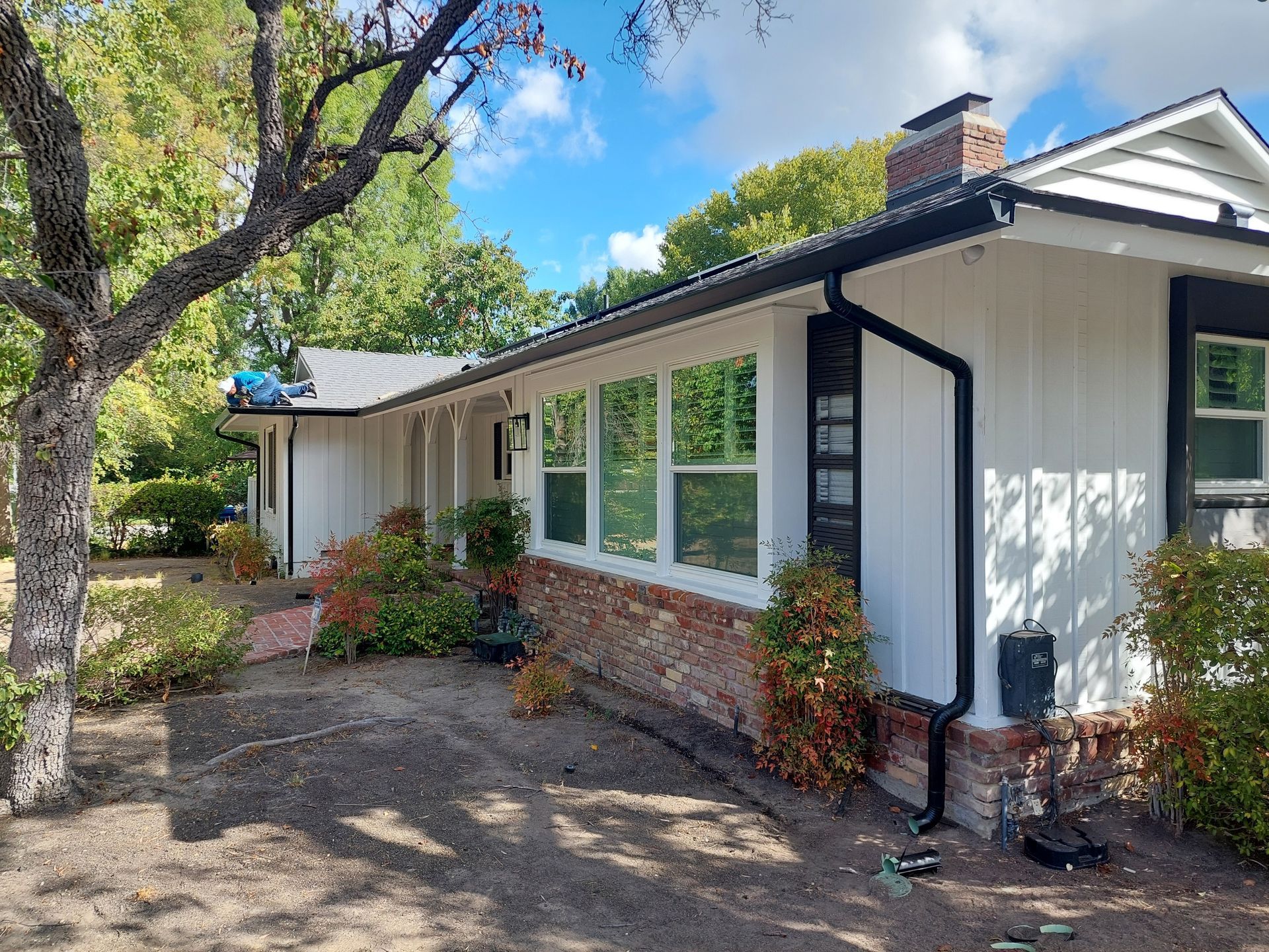 Single-story white house with brick trim, large windows, and a tree-shaded front yard