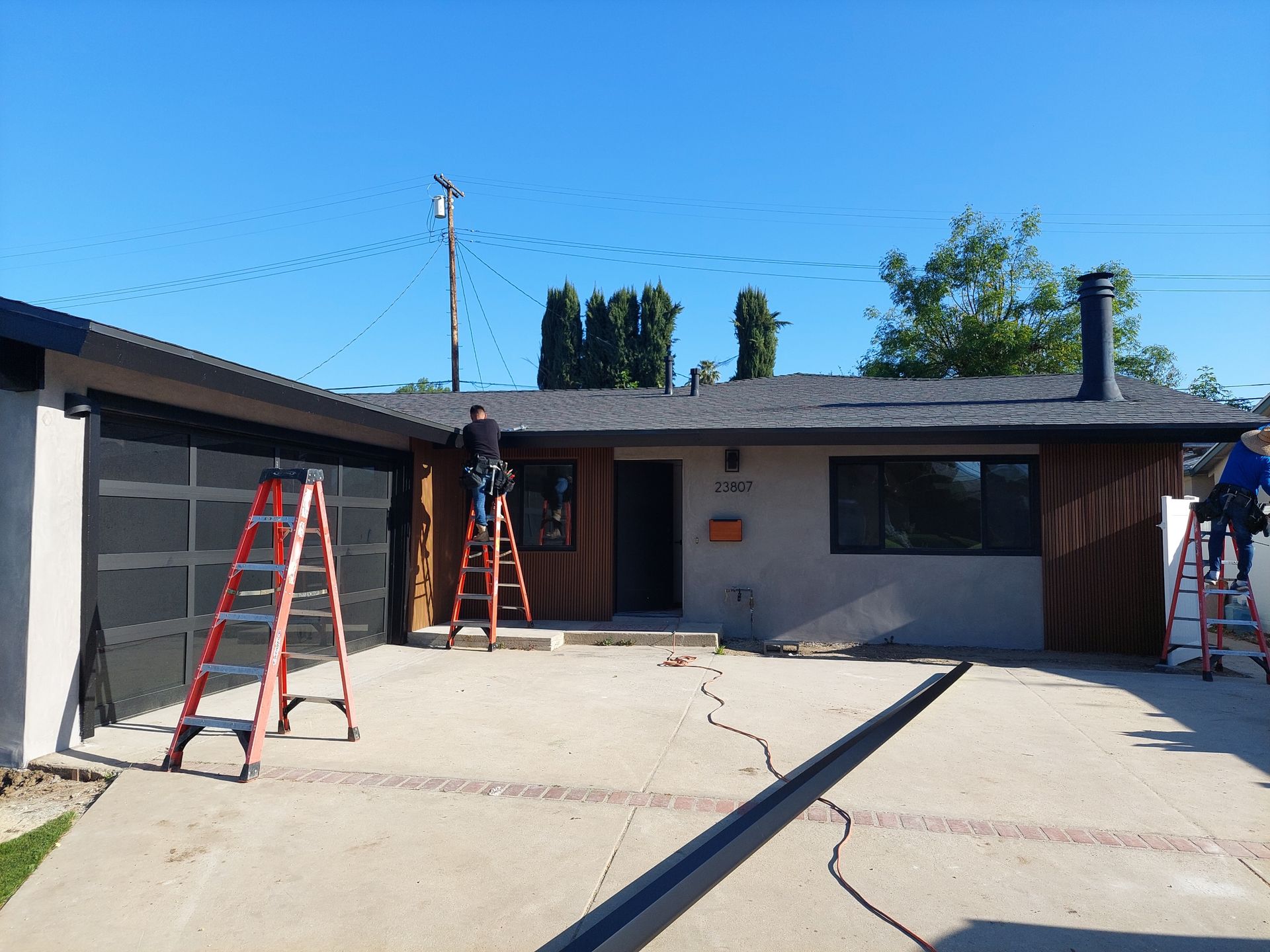 Single-story house with ladders set up in the driveway and roof, suggesting exterior repairs