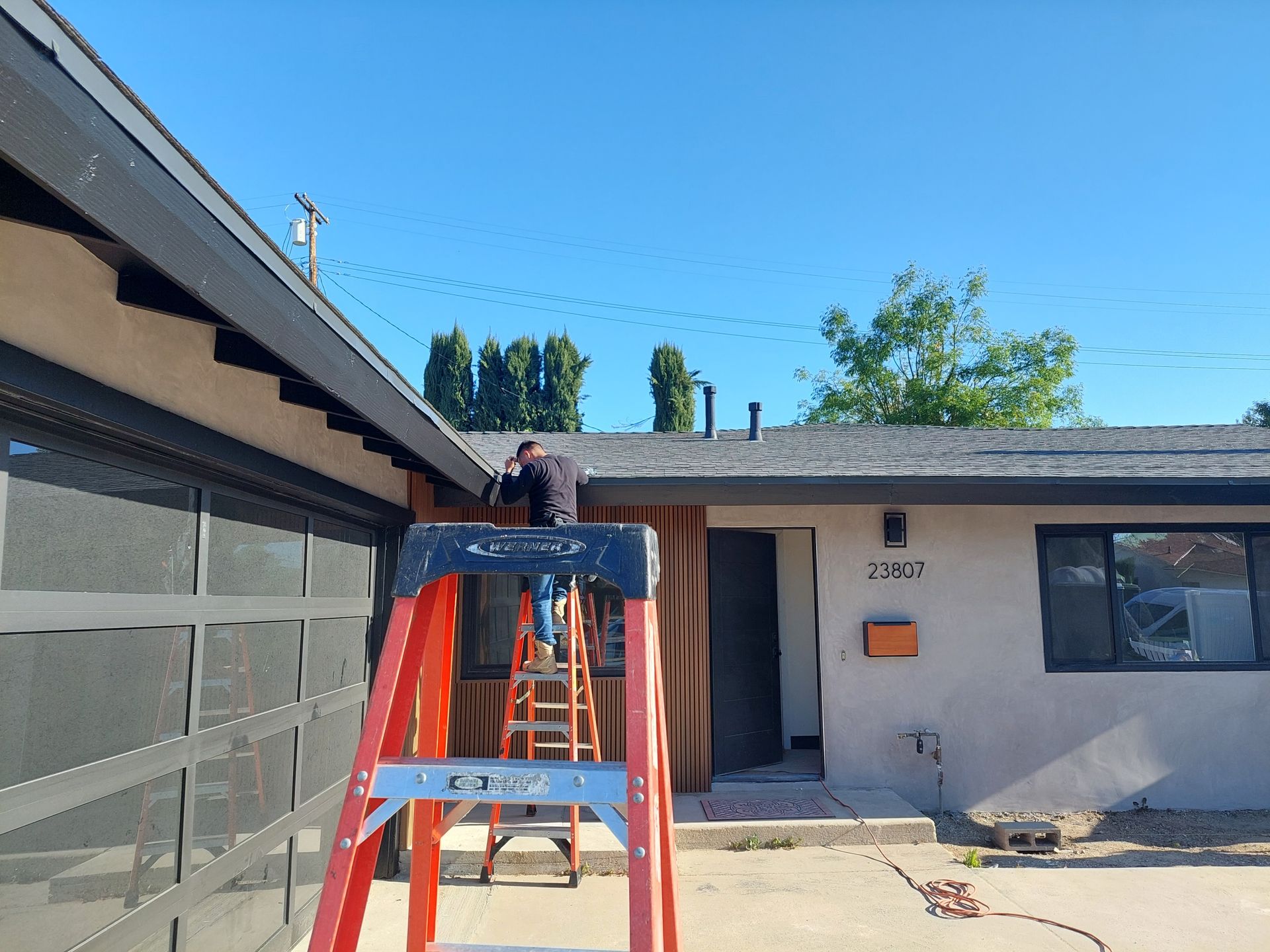 Worker on an orange ladder repairing a roof on a house in a sunny backyard