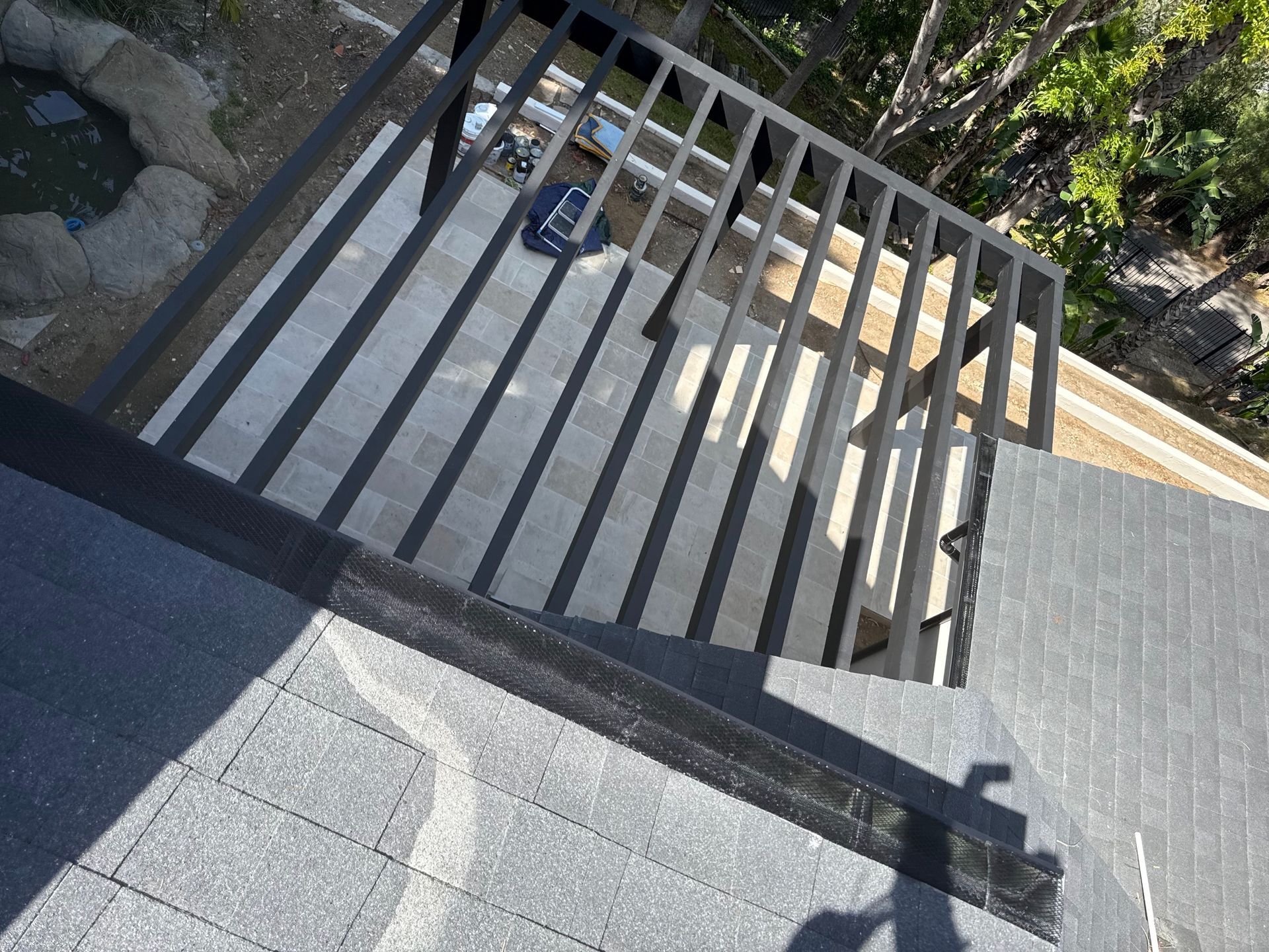 Outdoor stairway with gray railings beside a stone path and rooftop edge