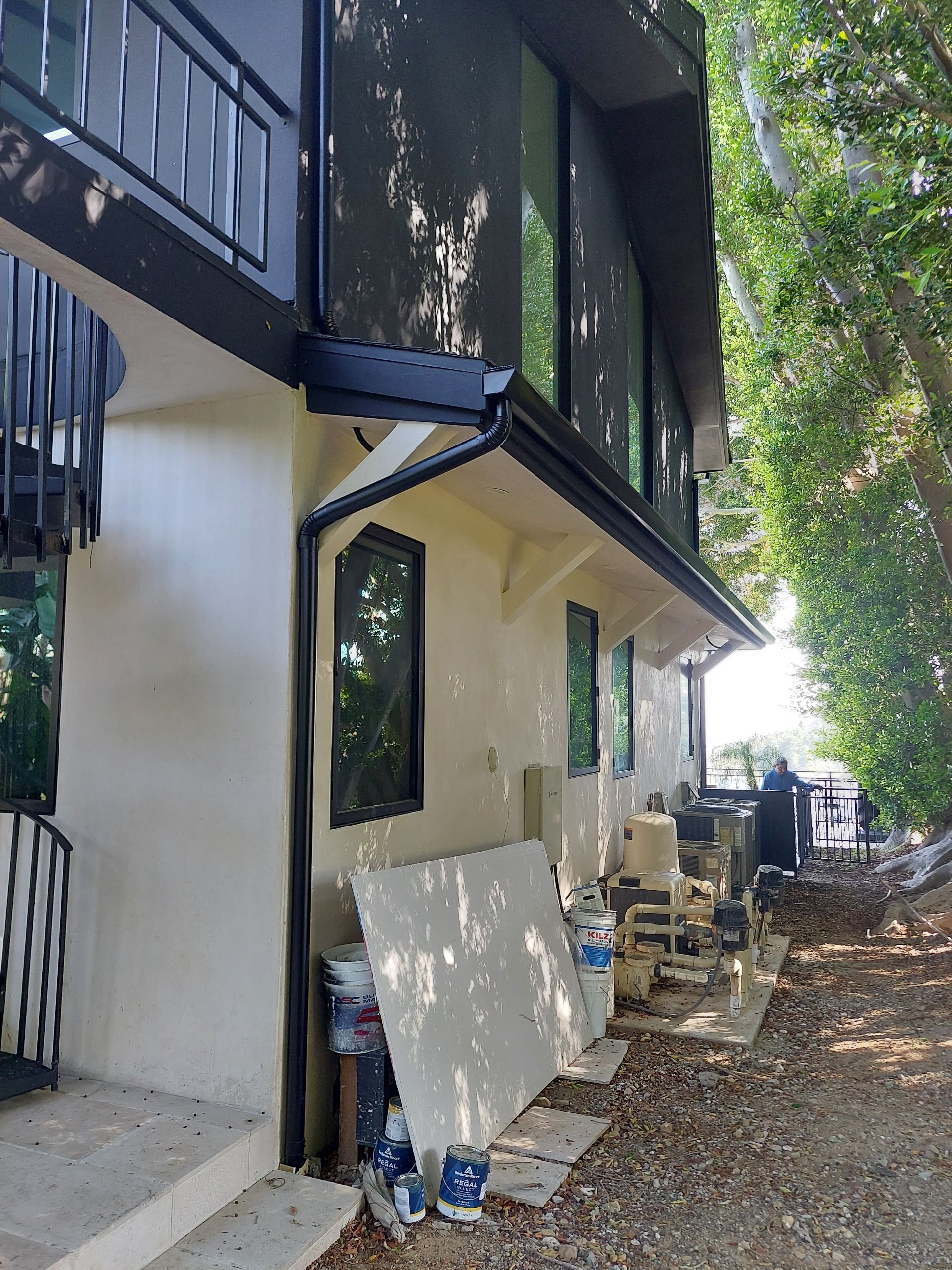 Exterior of a house with white walls, black balcony, and construction materials leaning against the side near a gravel path