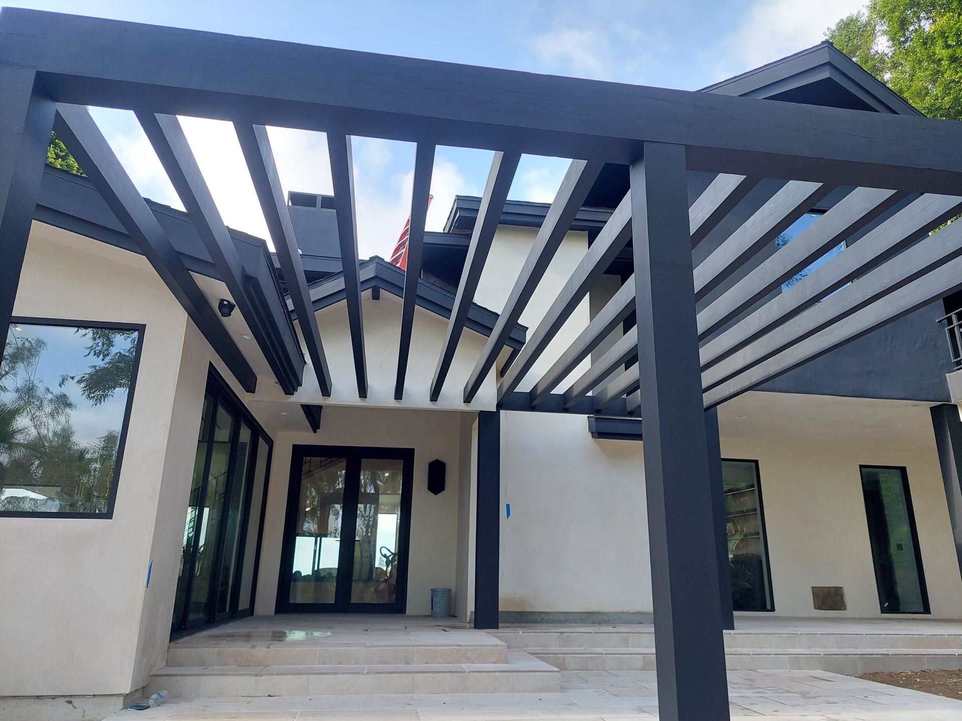 Modern house entrance with dark pergola beams over a front patio and glass double doors