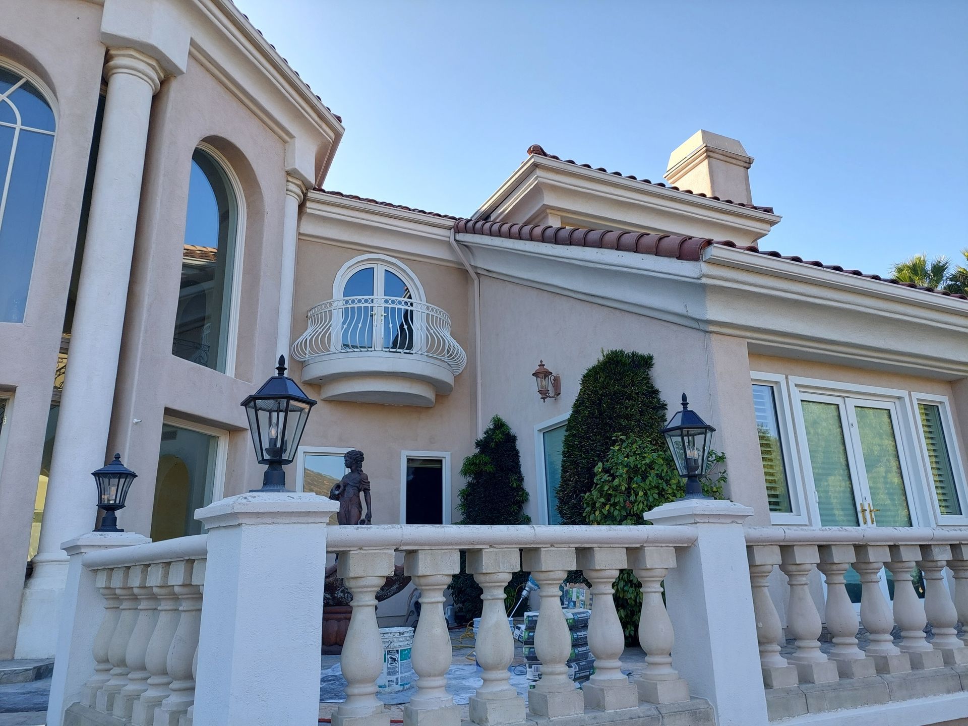 Elegant beige mansion with arched windows, balcony, and white stone balustrade under a blue sky