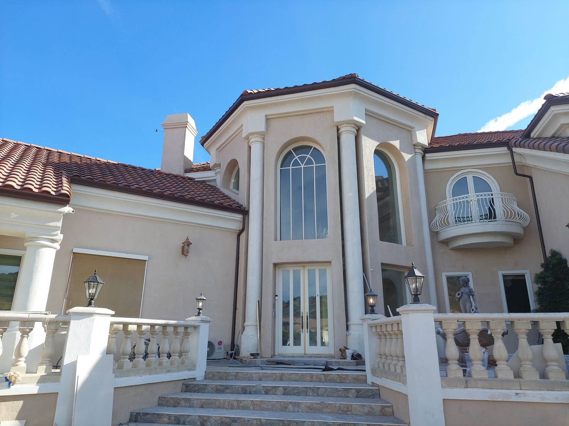 Luxury Mediterranean-style house with arched entry, tall windows, and stone steps under a blue sky