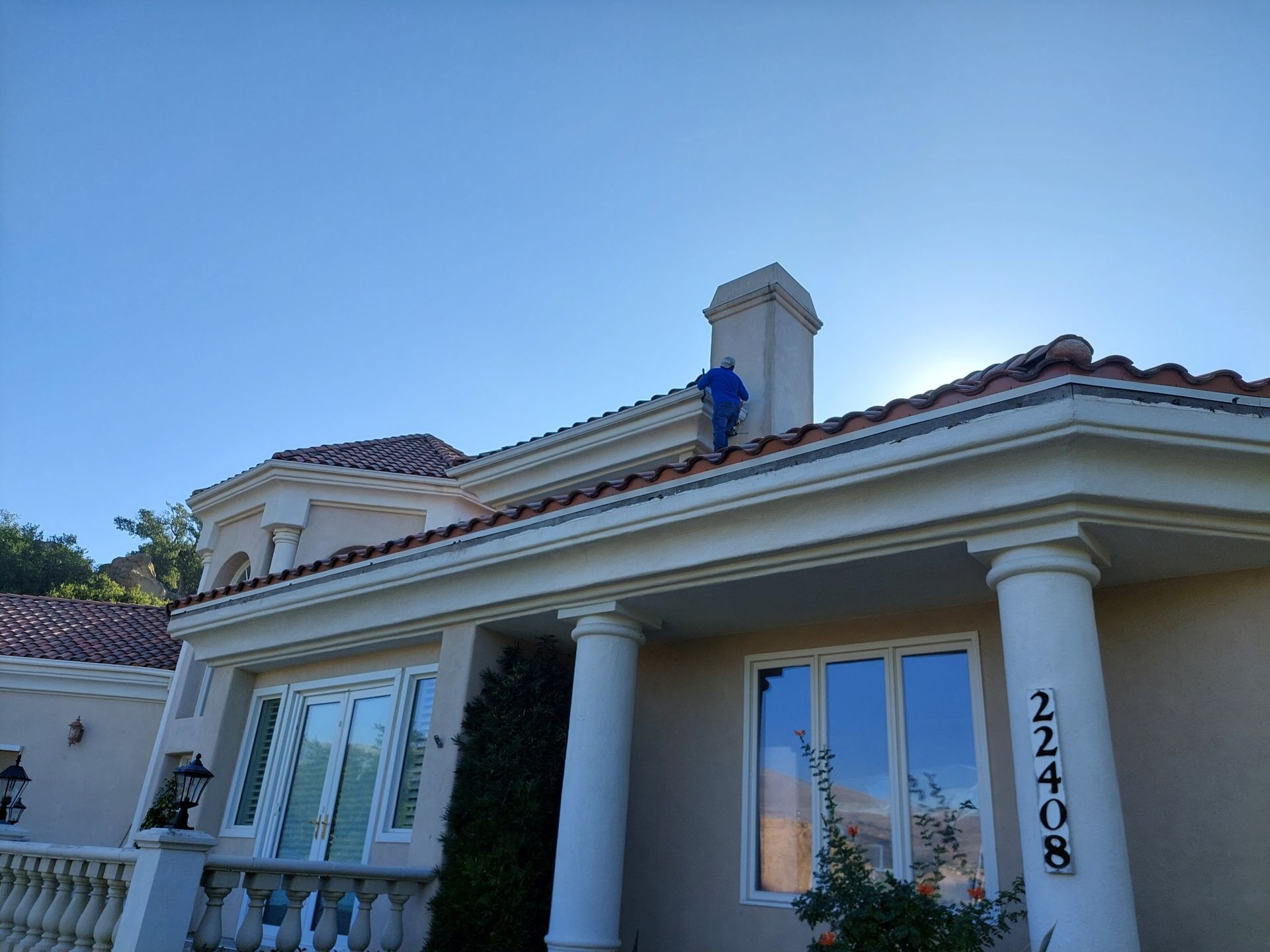 House exterior with white columns and red-tile roof, viewed from below against a clear blue sky.