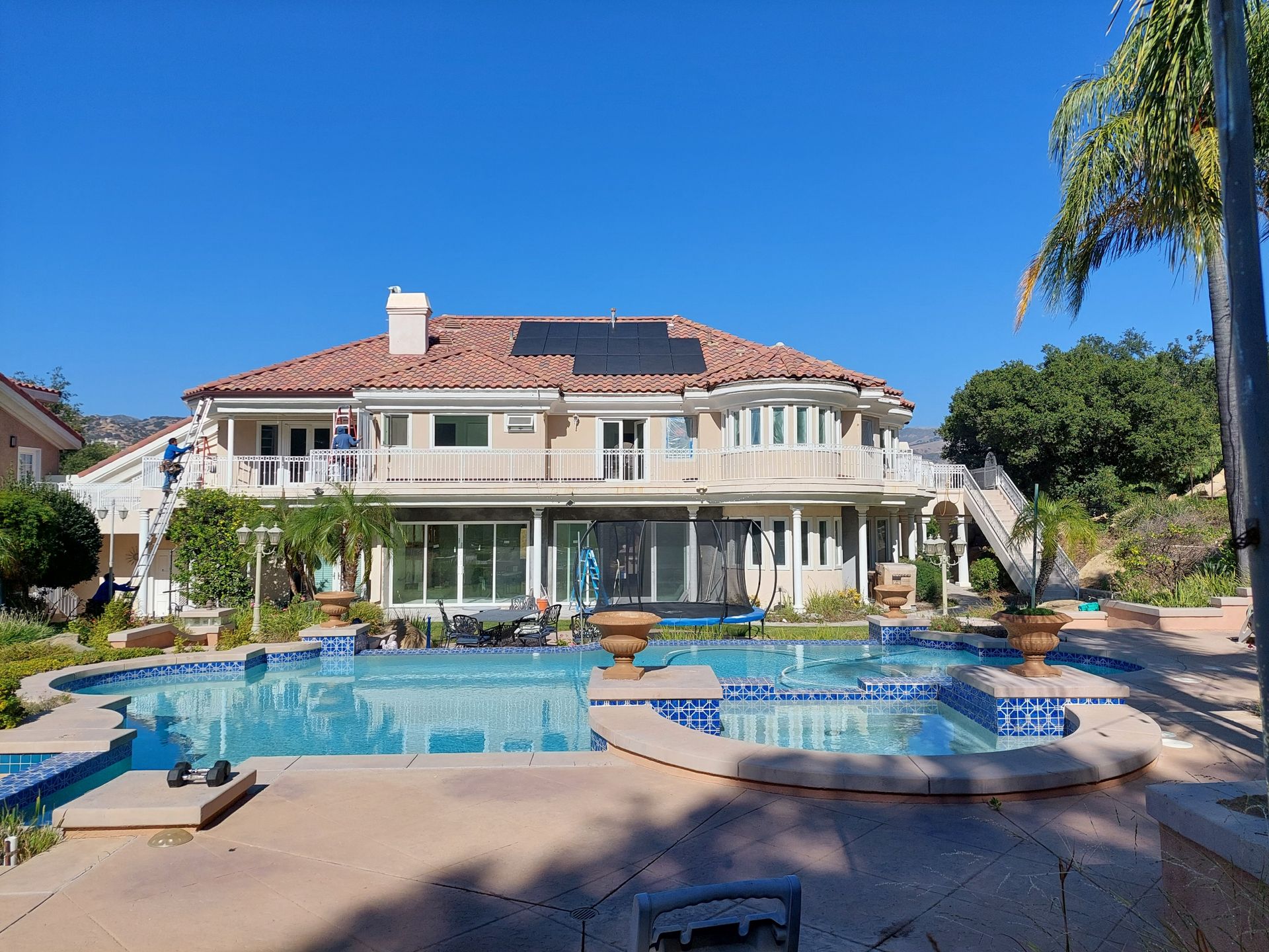 Large Mediterranean-style house with a blue swimming pool and palm trees under a clear sky