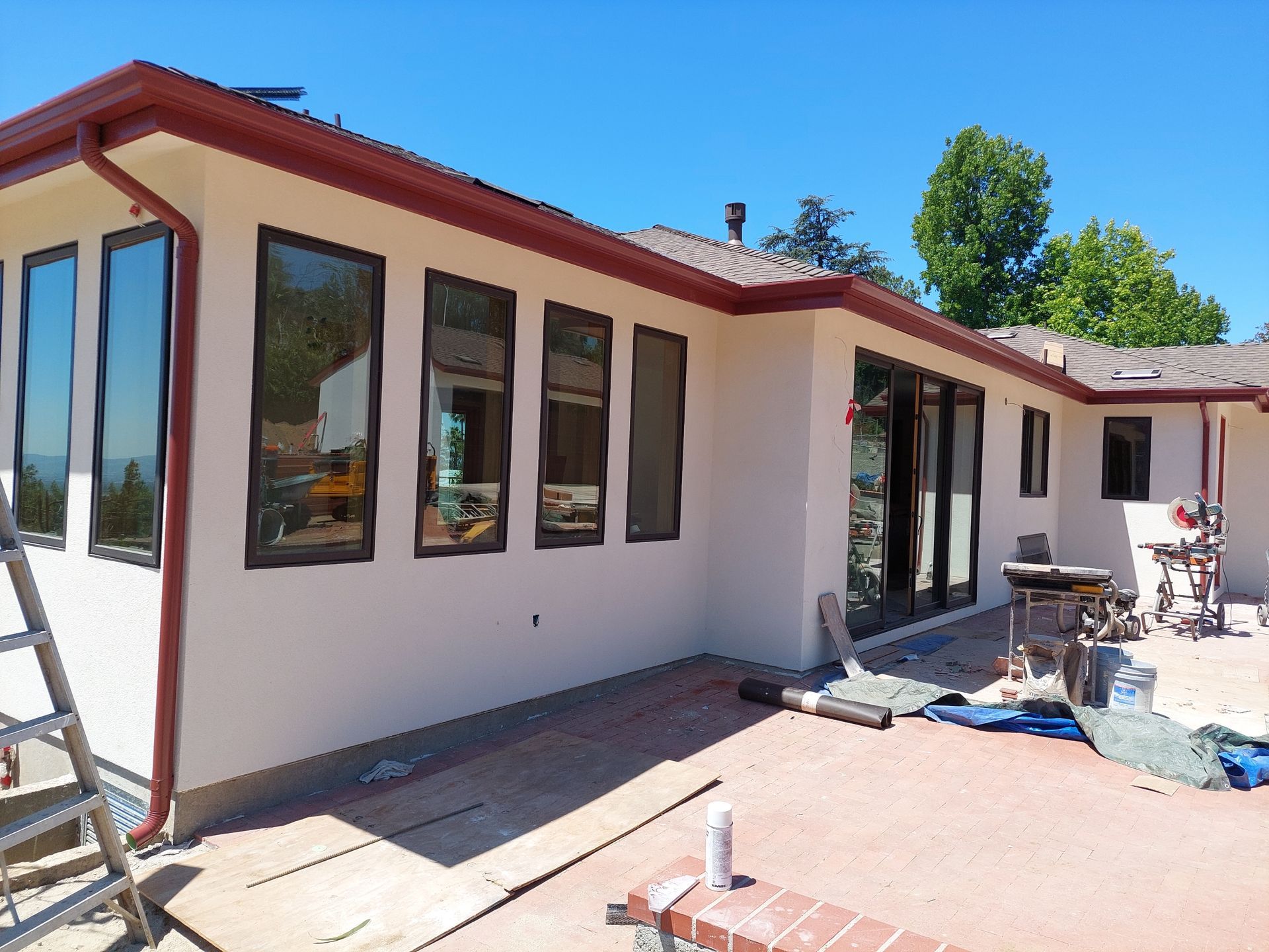 Single-story house exterior with white walls, dark trim, and a patio under construction