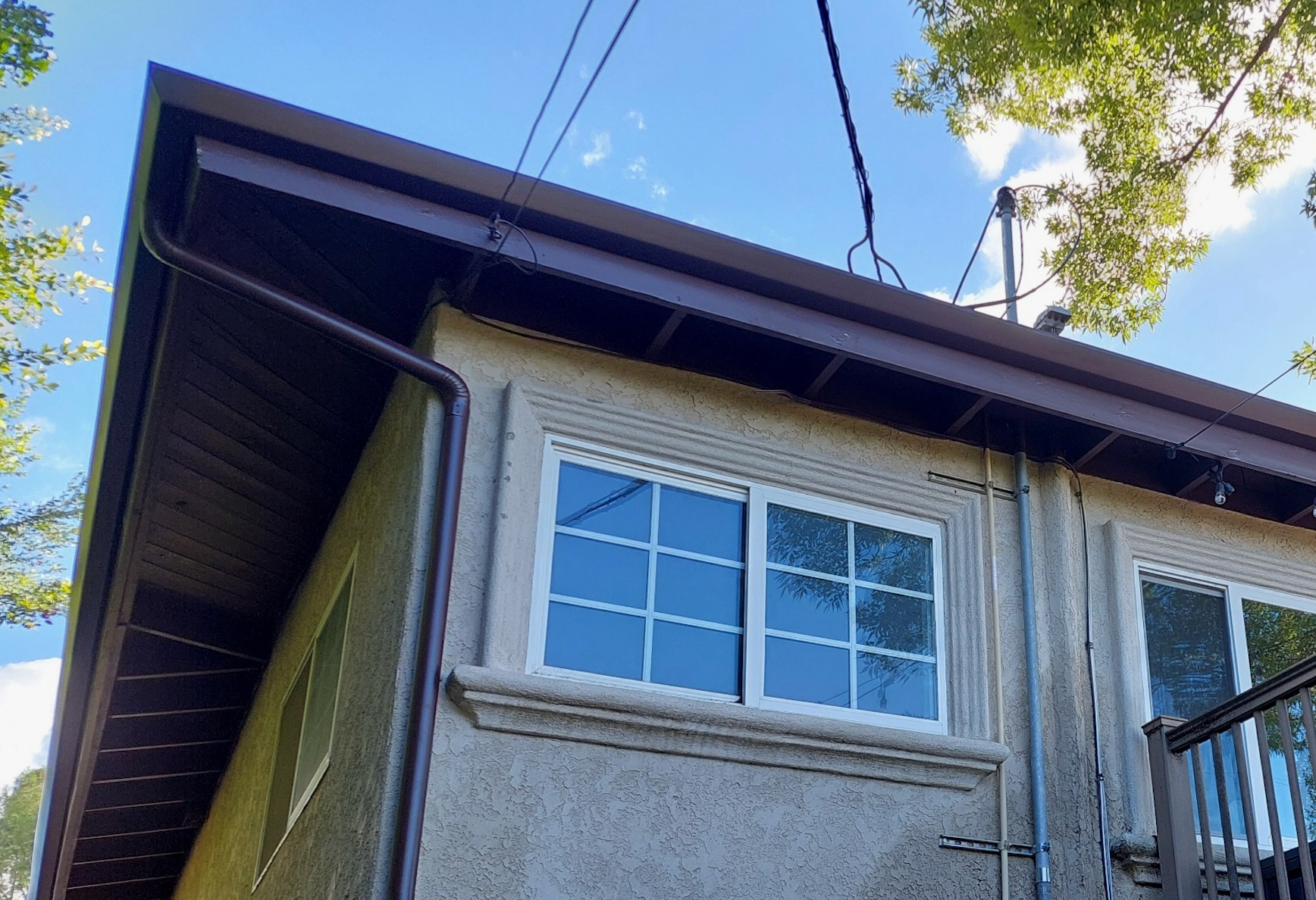 Side view of a house with beige stucco, white windows, and overhead power lines against a blue sky.