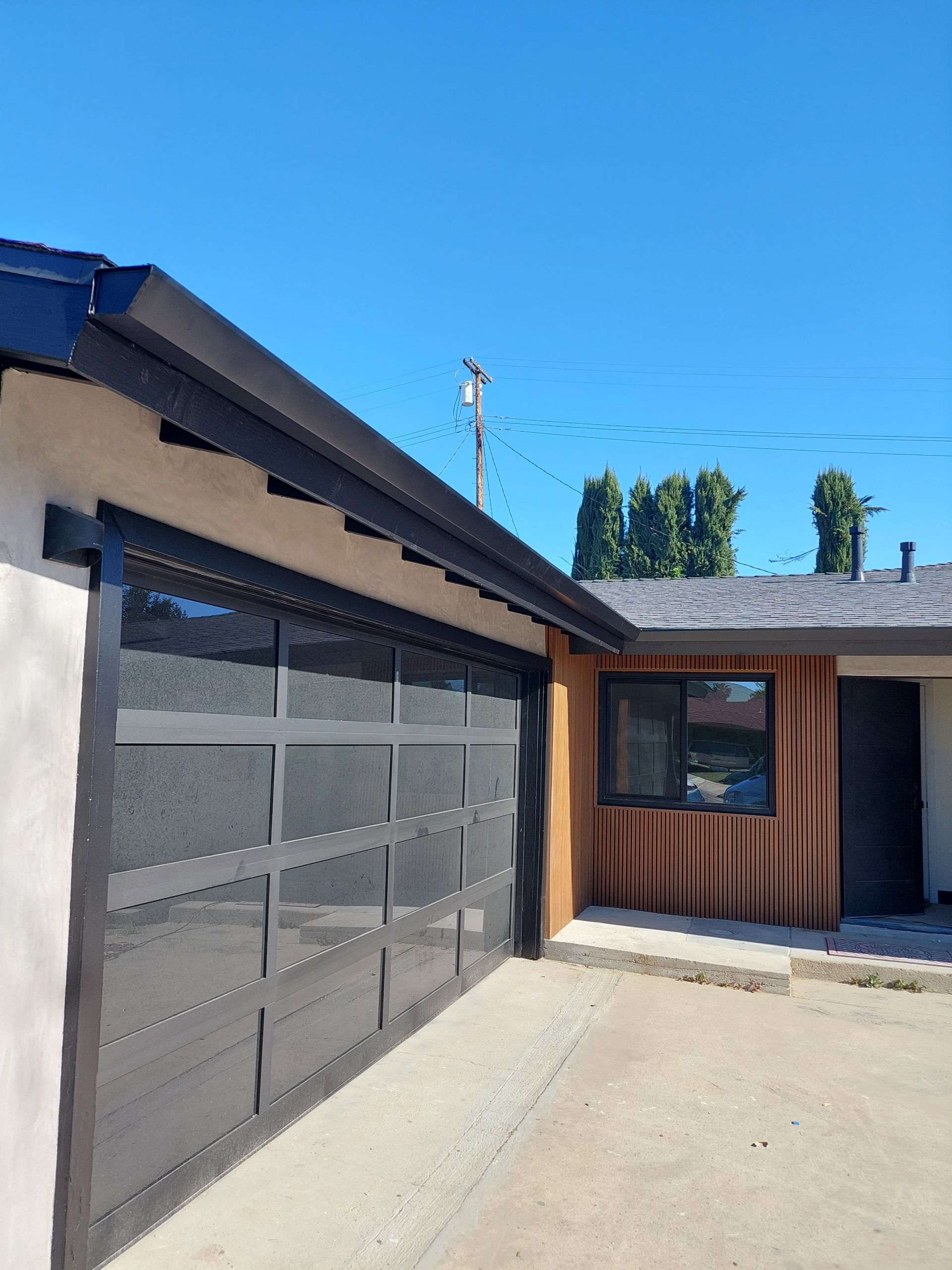 Modern garage and front entry with dark garage door, wood siding, and blue sky