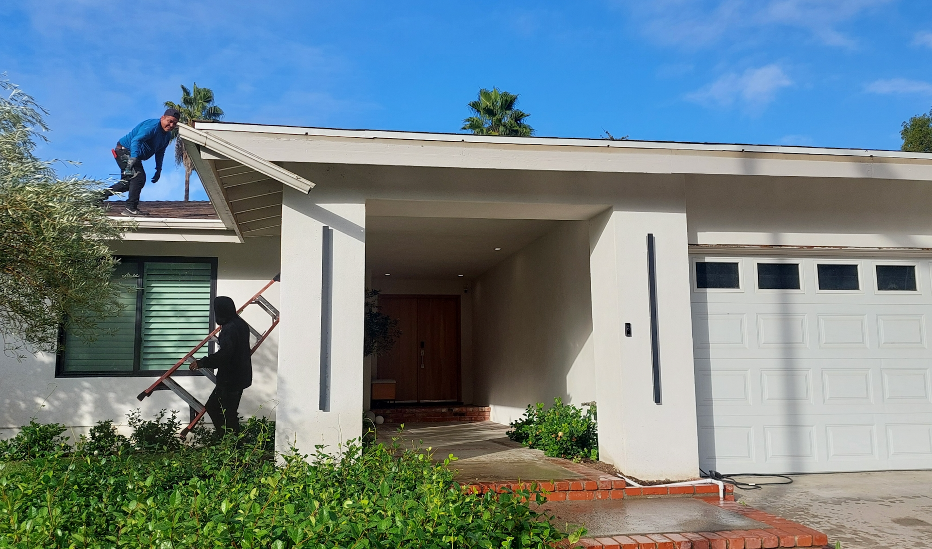 Single-story house with white exterior, garage, front porch, and green shrubs under a blue sky