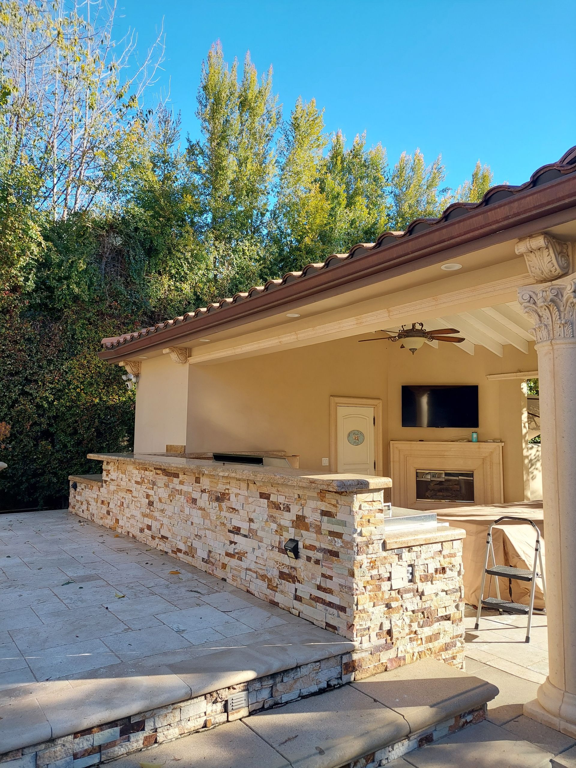 Outdoor patio with stone wall, beige house exterior, and trees under a clear blue sky