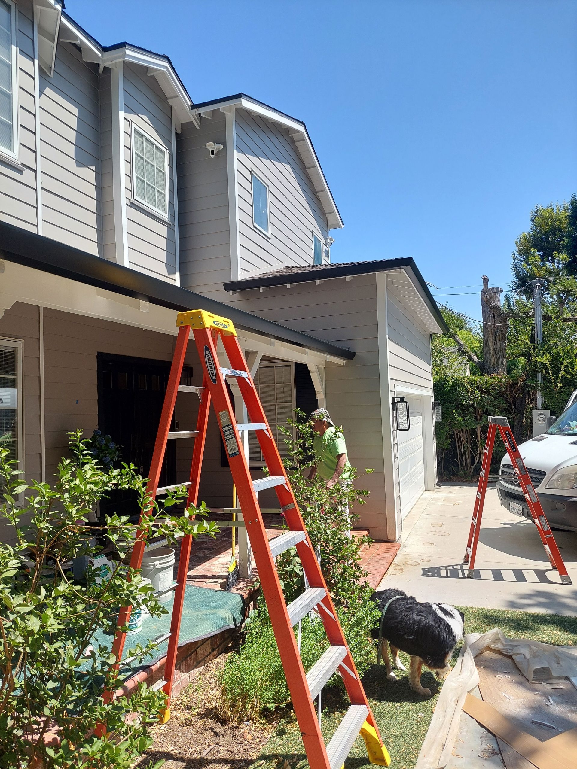 Two orange ladders outside a suburban house with workers and tools in a sunlit driveway