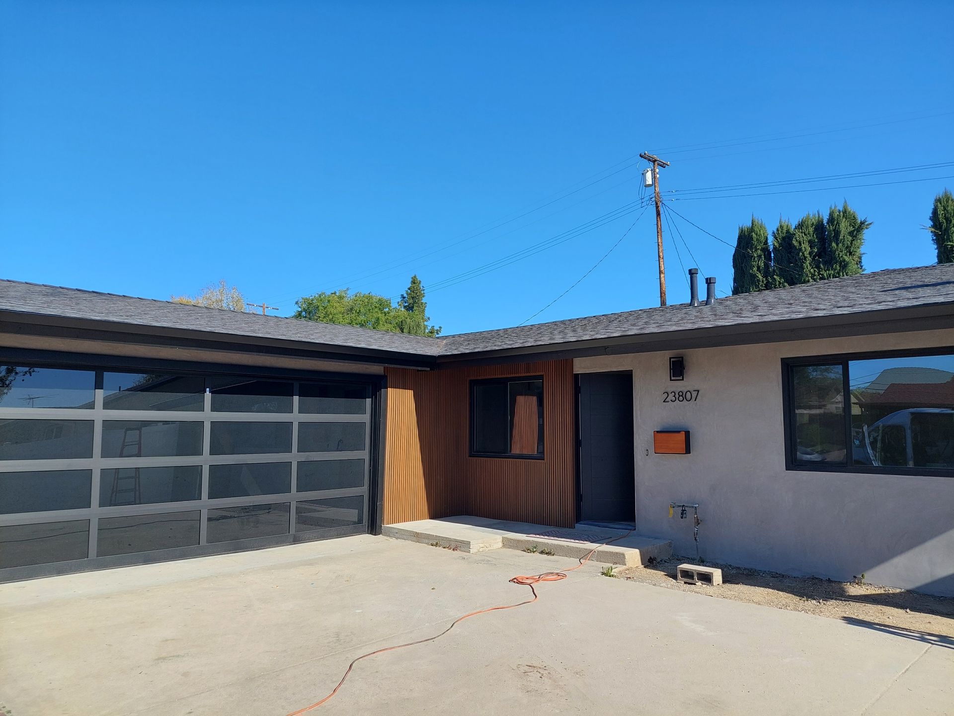 Single-story house exterior with gray garage door, wooden front door, and bright blue sky