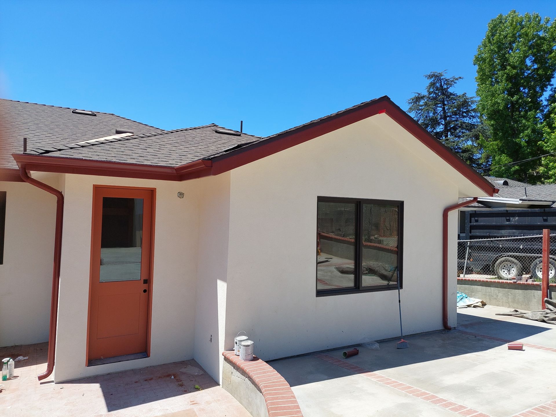 Small white stucco house with red trim, orange door, and a window under a clear blue sky.