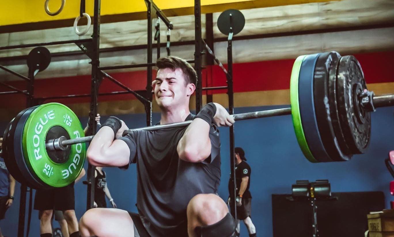 A man is squatting with a barbell over his head in a gym.