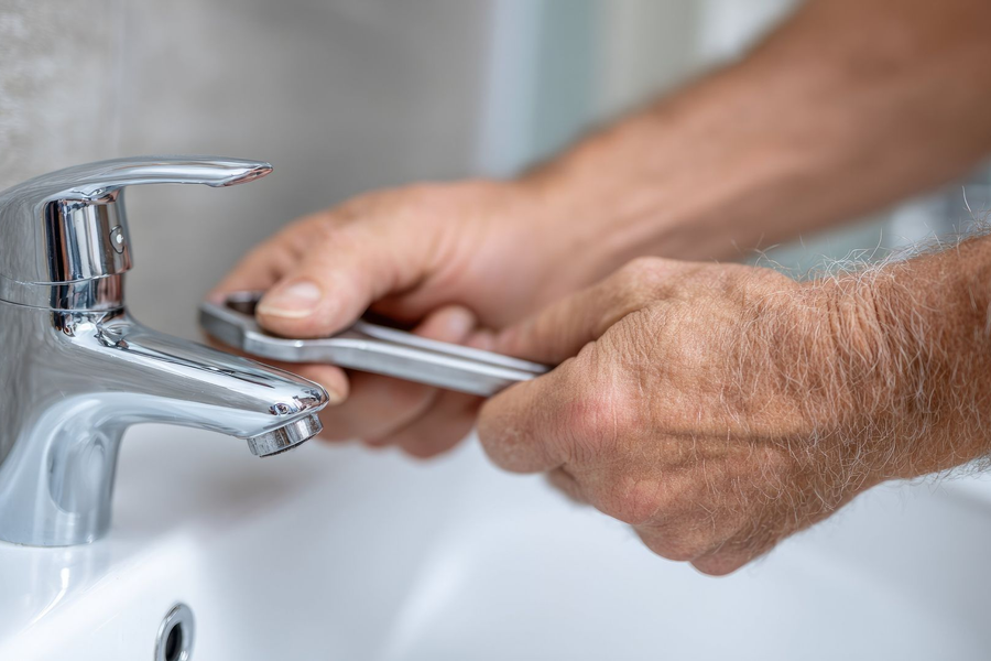 Hands using a wrench to tighten a chrome bathroom faucet.