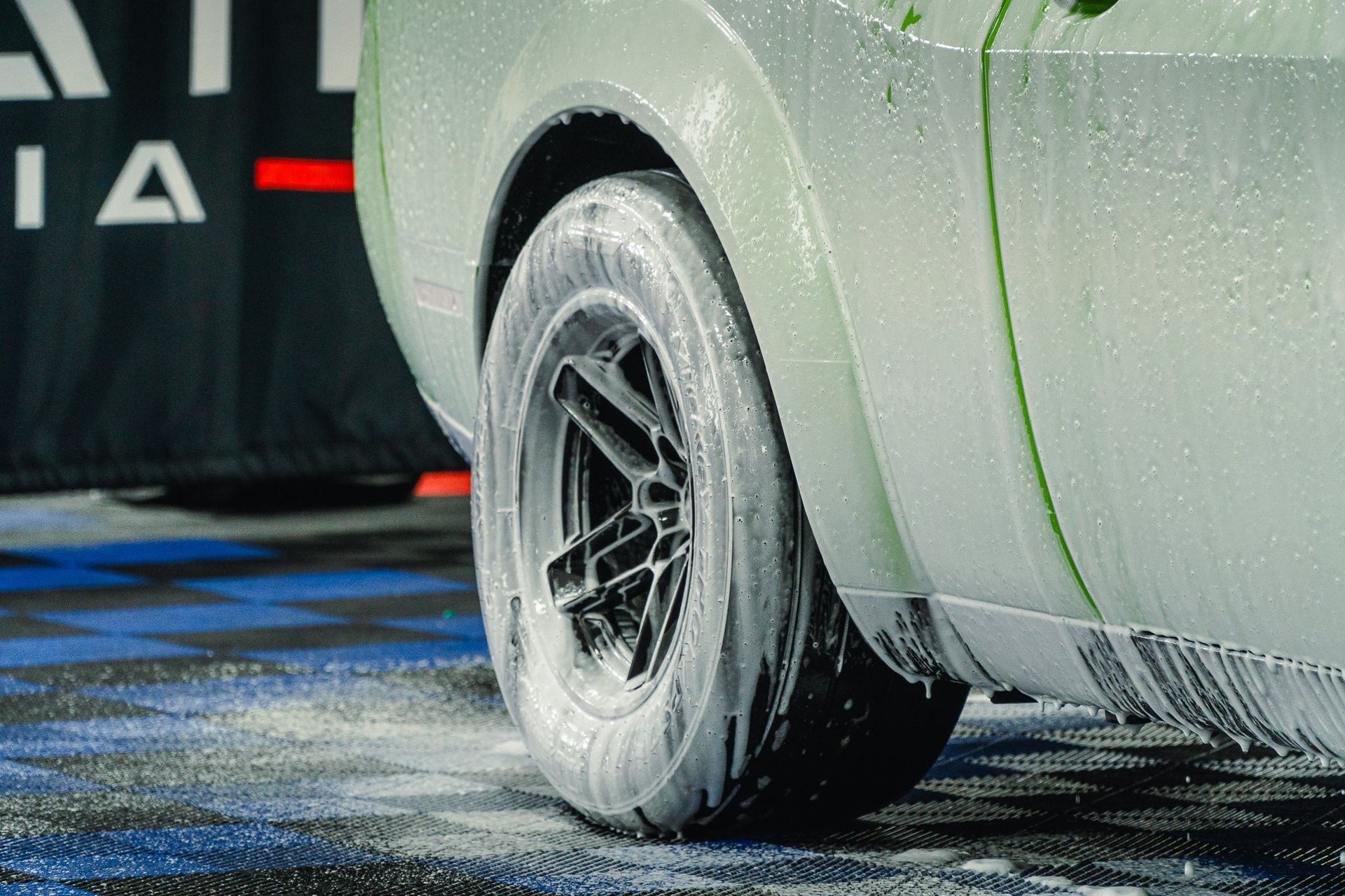Close-up of a car wheel on a wet track, with tire spray and blue markings on the ground.
