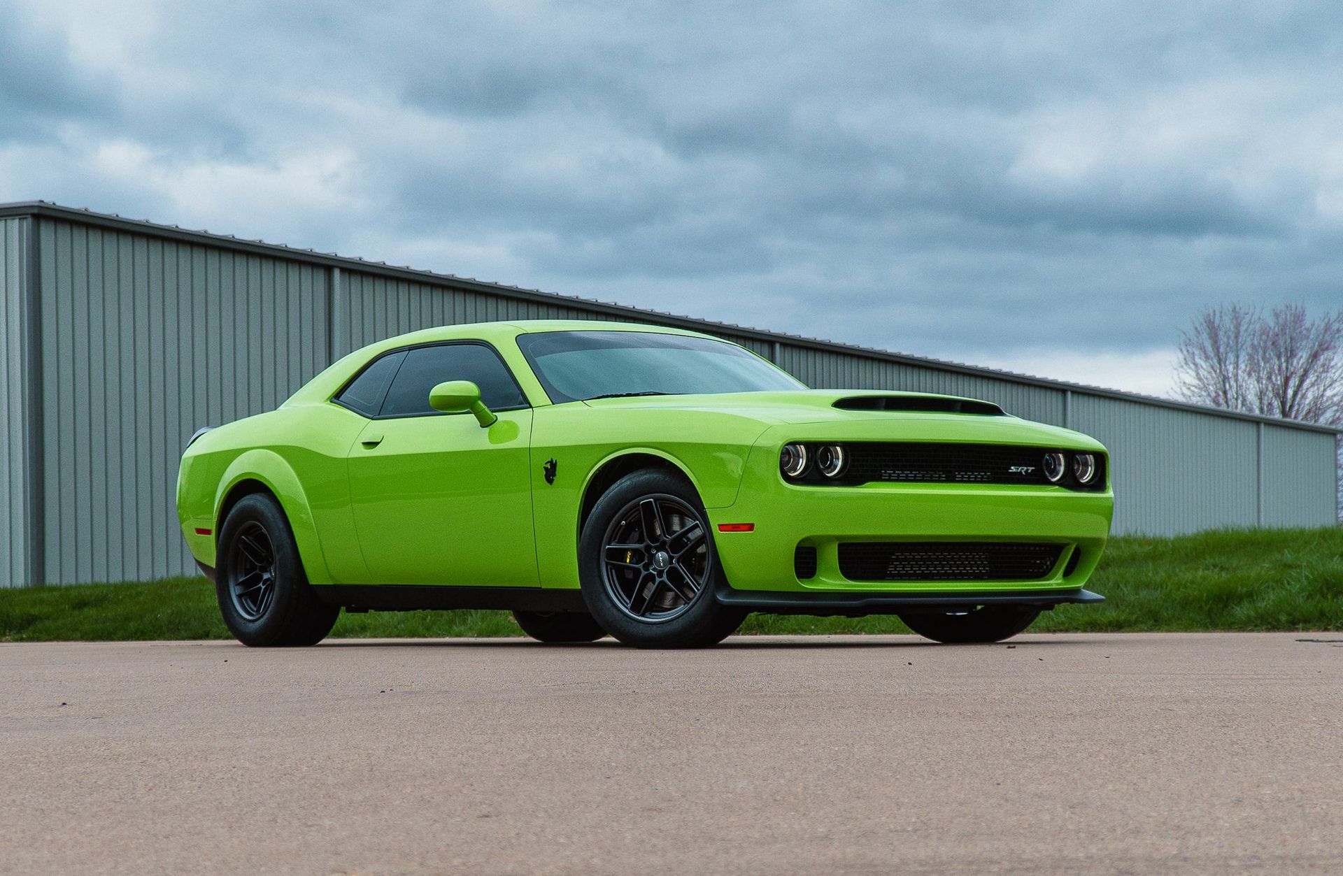 Bright green Dodge Challenger parked on a paved lot beside a metal building under a cloudy sky