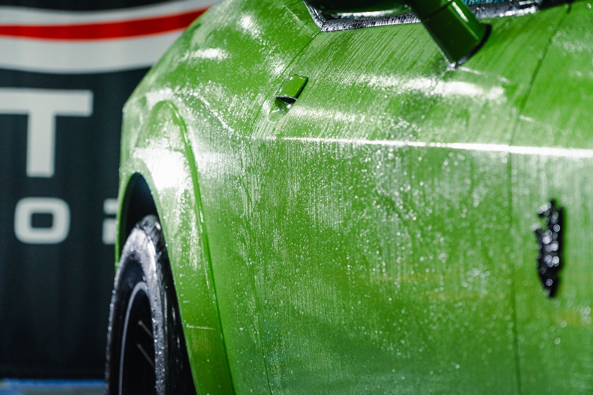 Close-up of a green sports car covered in water droplets, with a blurred striped background