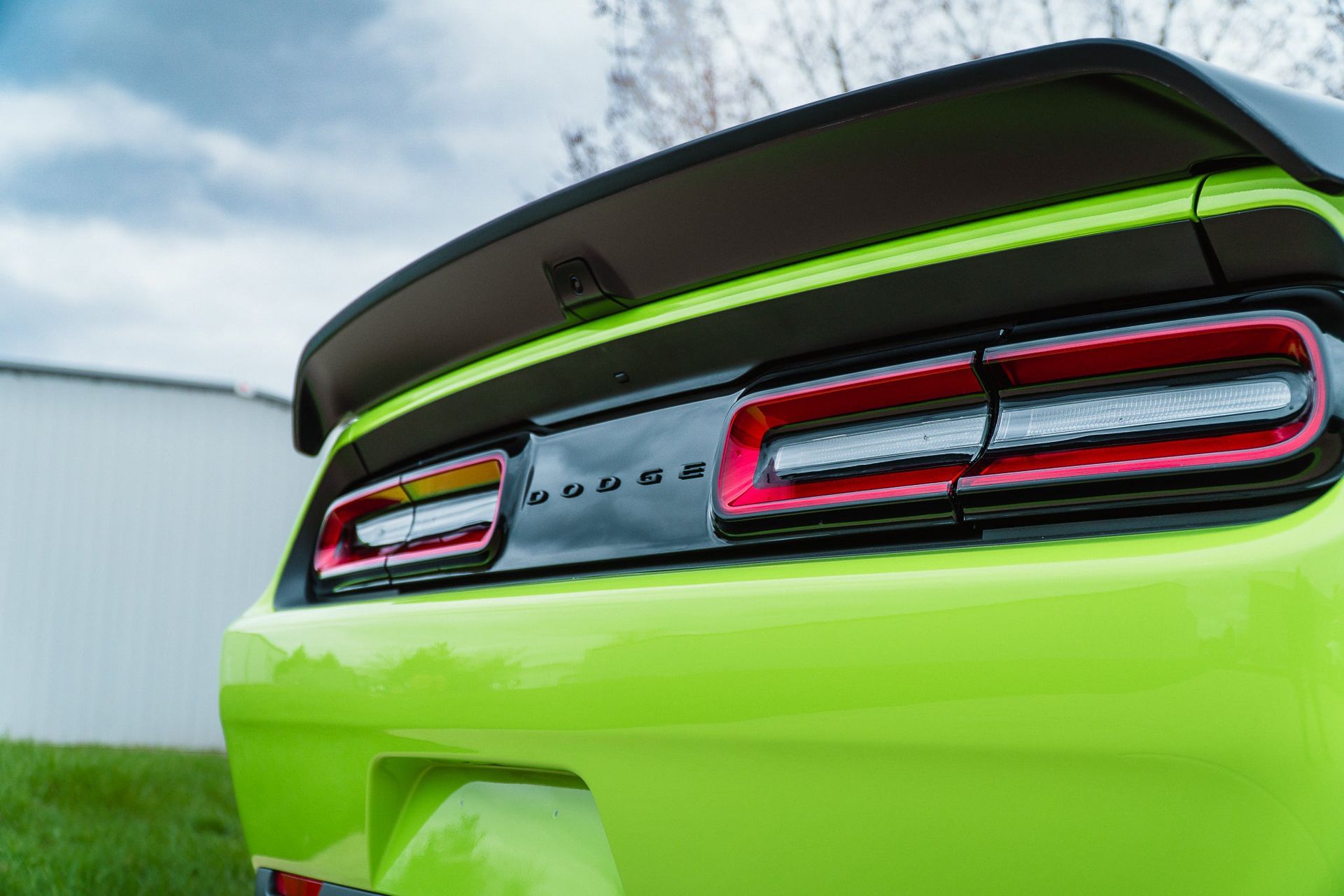 Rear view of a bright lime green Dodge sports car with illuminated taillights and a spoiler