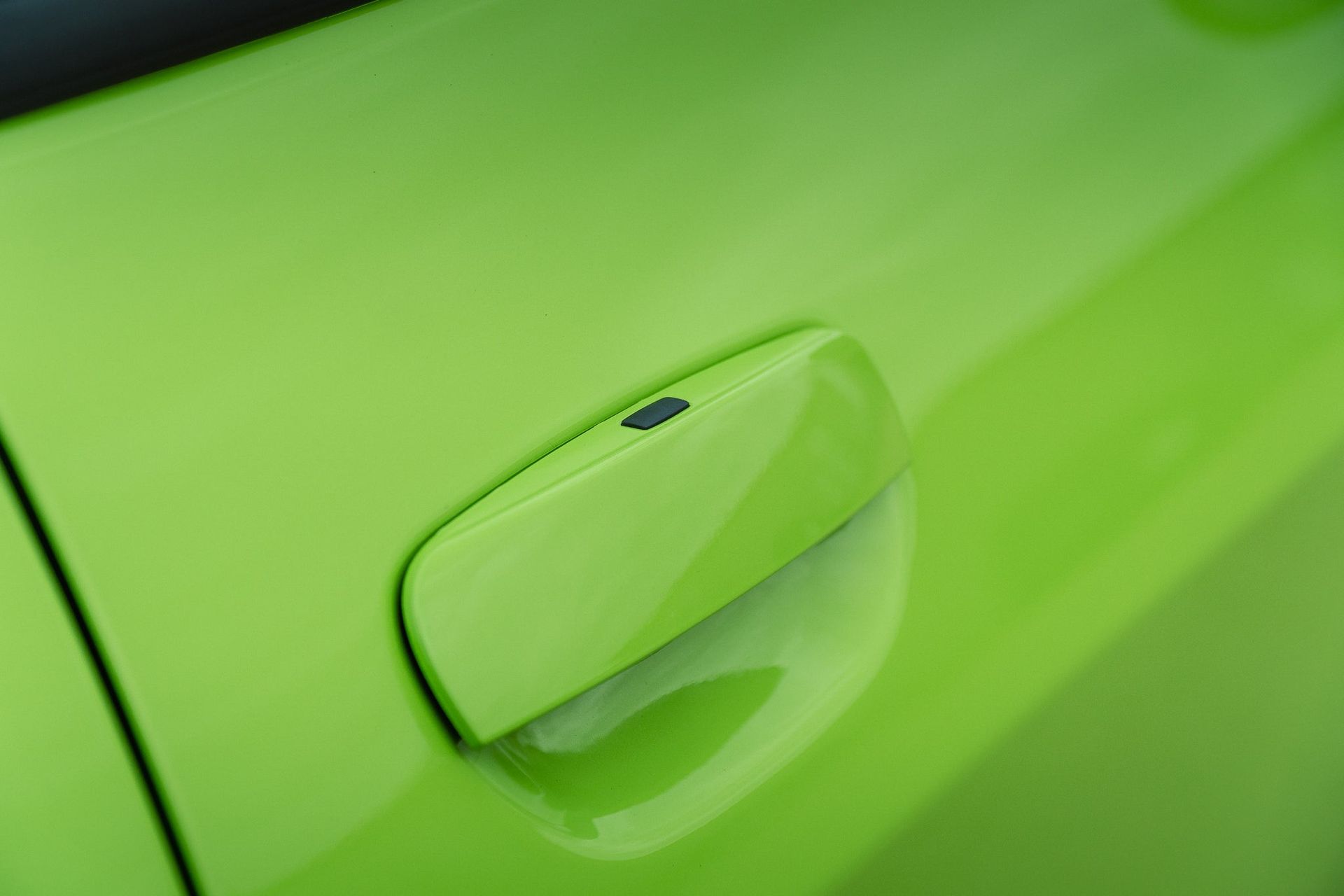 Close-up of a bright green car door handle on a matching green vehicle body