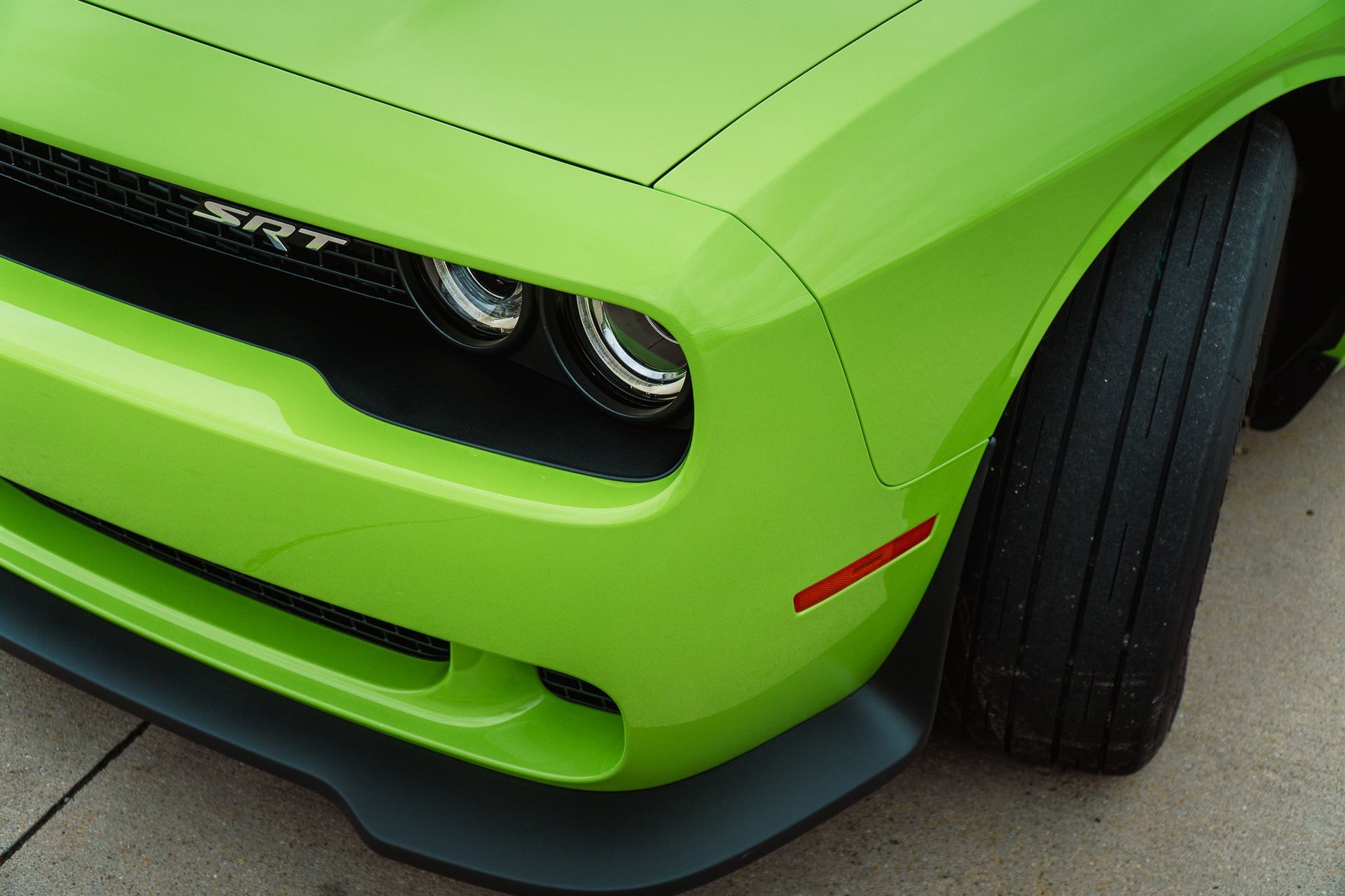 Bright green sports car front corner with headlights and black splitter on pavement