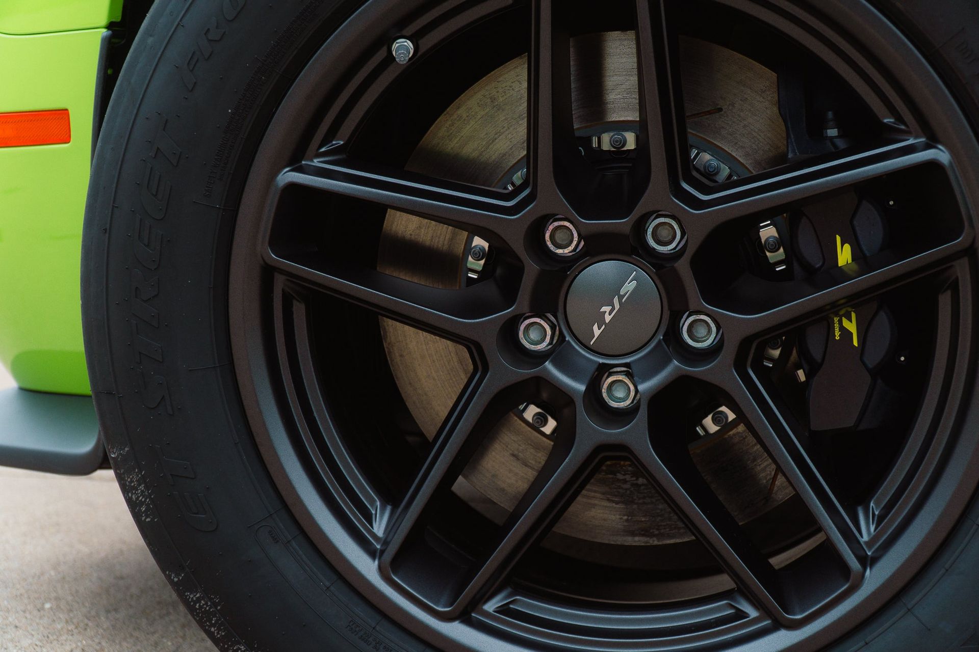 Close-up of a black sports car wheel with a yellow brake caliper and green body panel