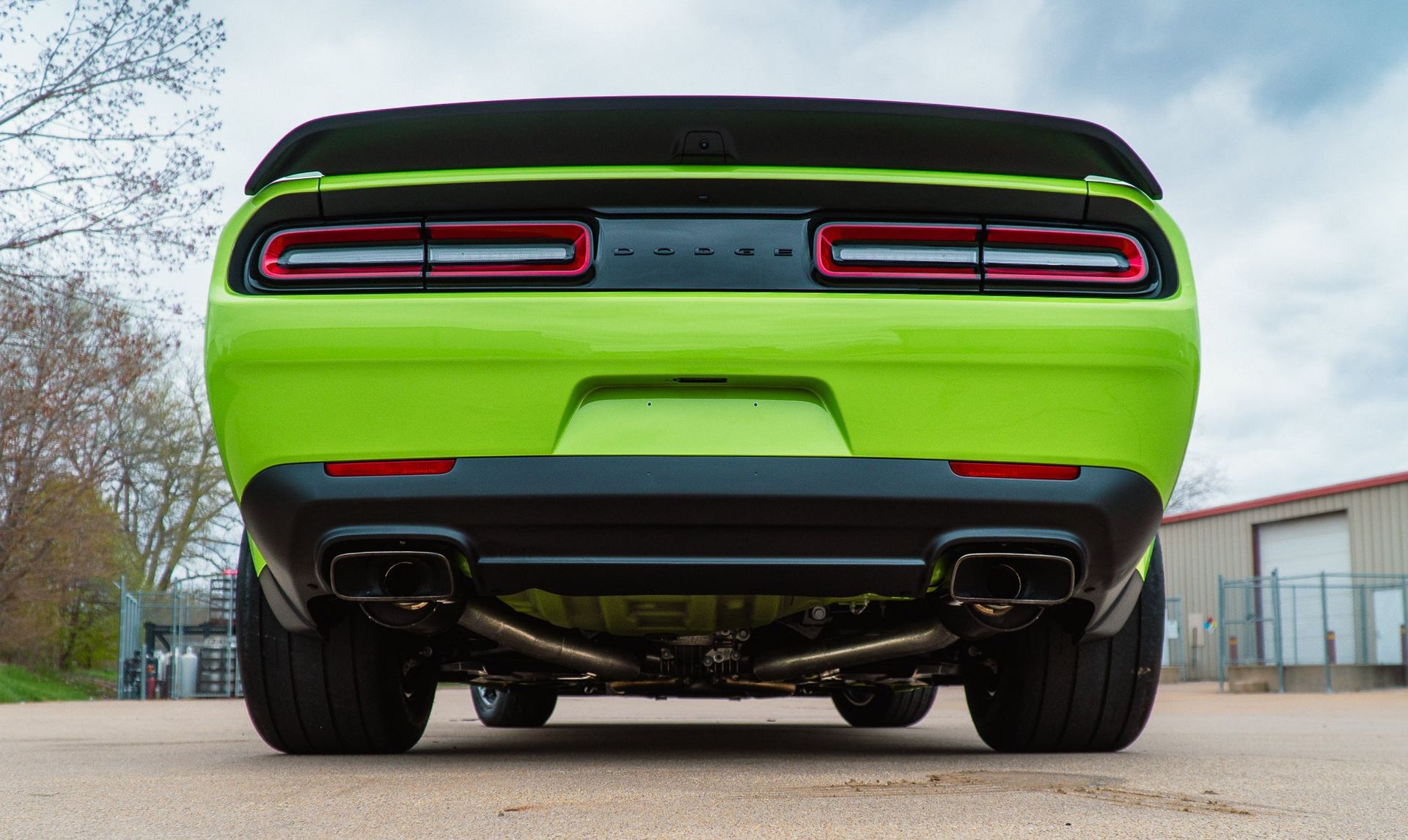 Rear view of a bright green sports car with black spoiler and dual exhausts, parked outdoors.