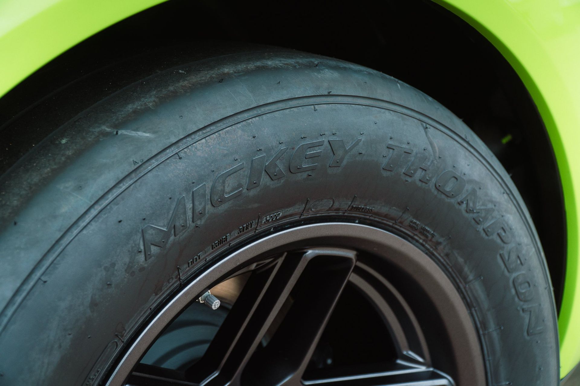 Close-up of a car tire and black wheel rim under a bright green fender.