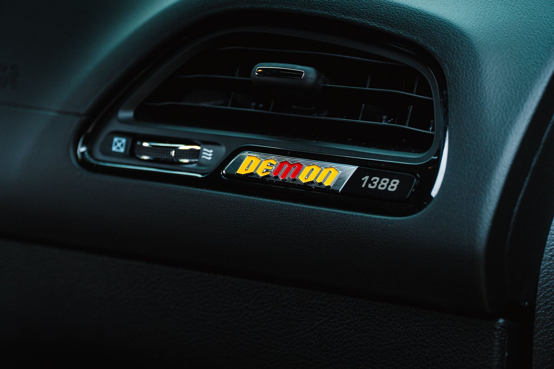 Car dashboard close-up with a vent-mounted digital display and colorful sticker reading “DEMON”