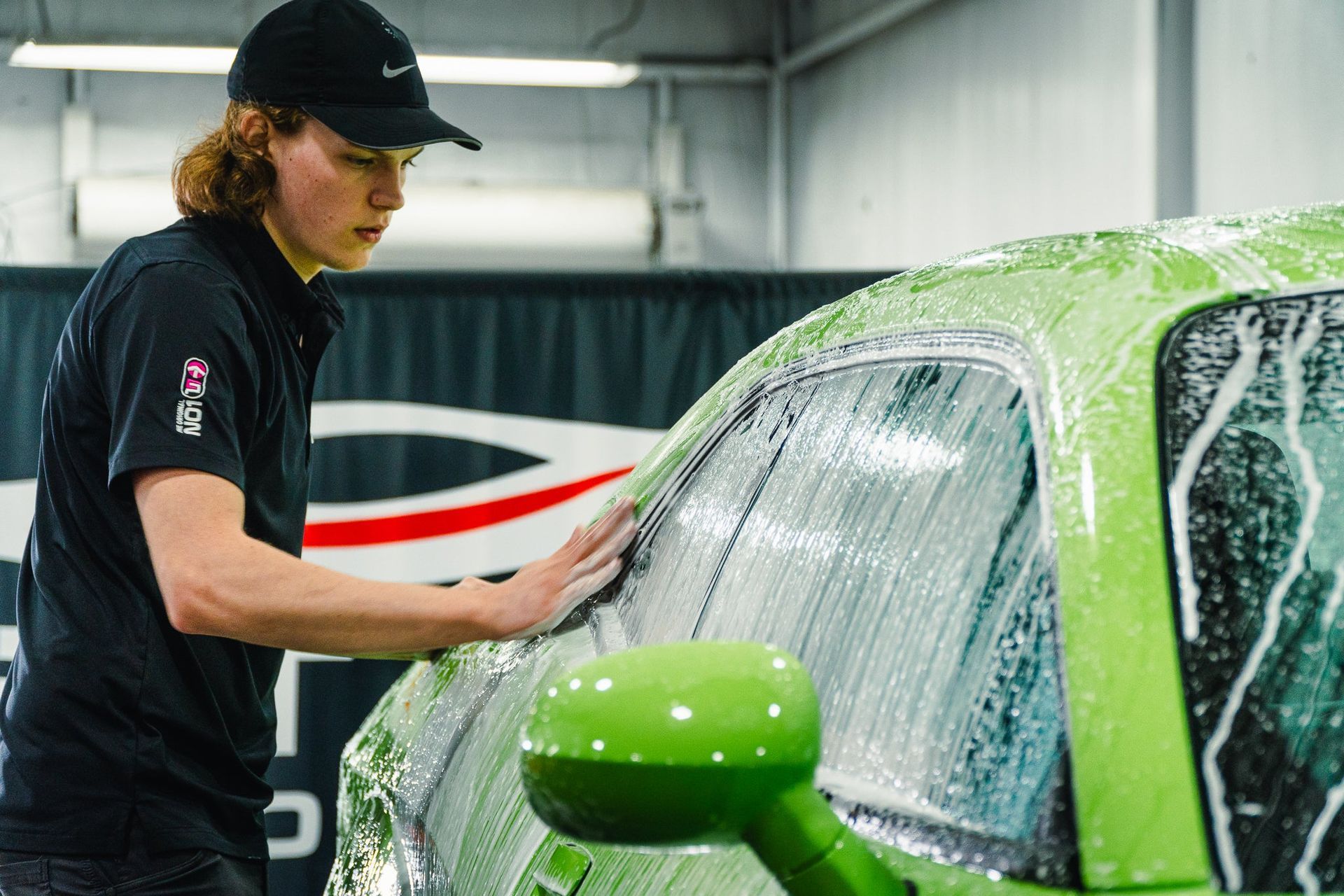 Detailing a bright green car while a person wipes the windshield with soap in a garage