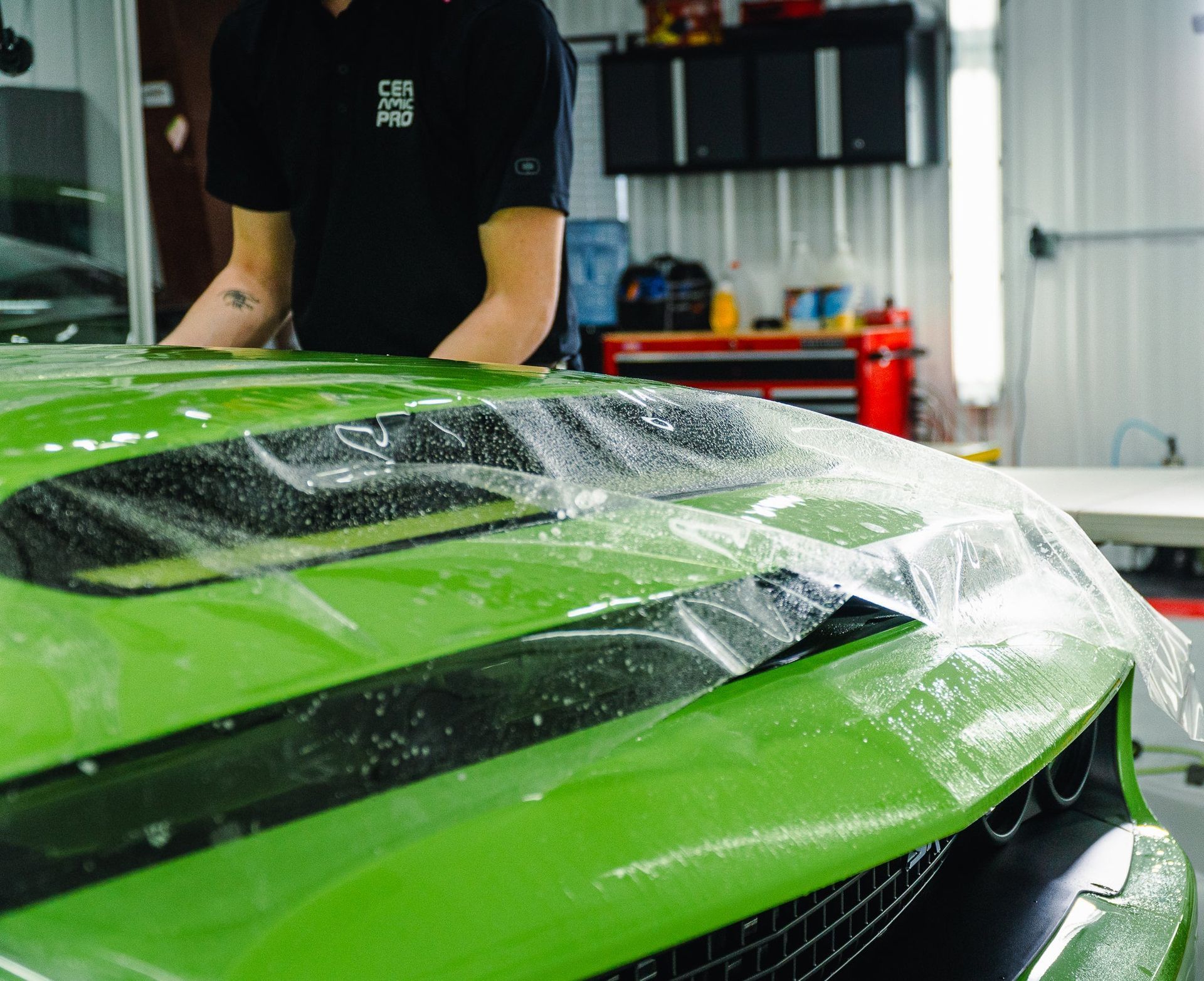 Green sports car hood being wrapped in clear protective film in a workshop