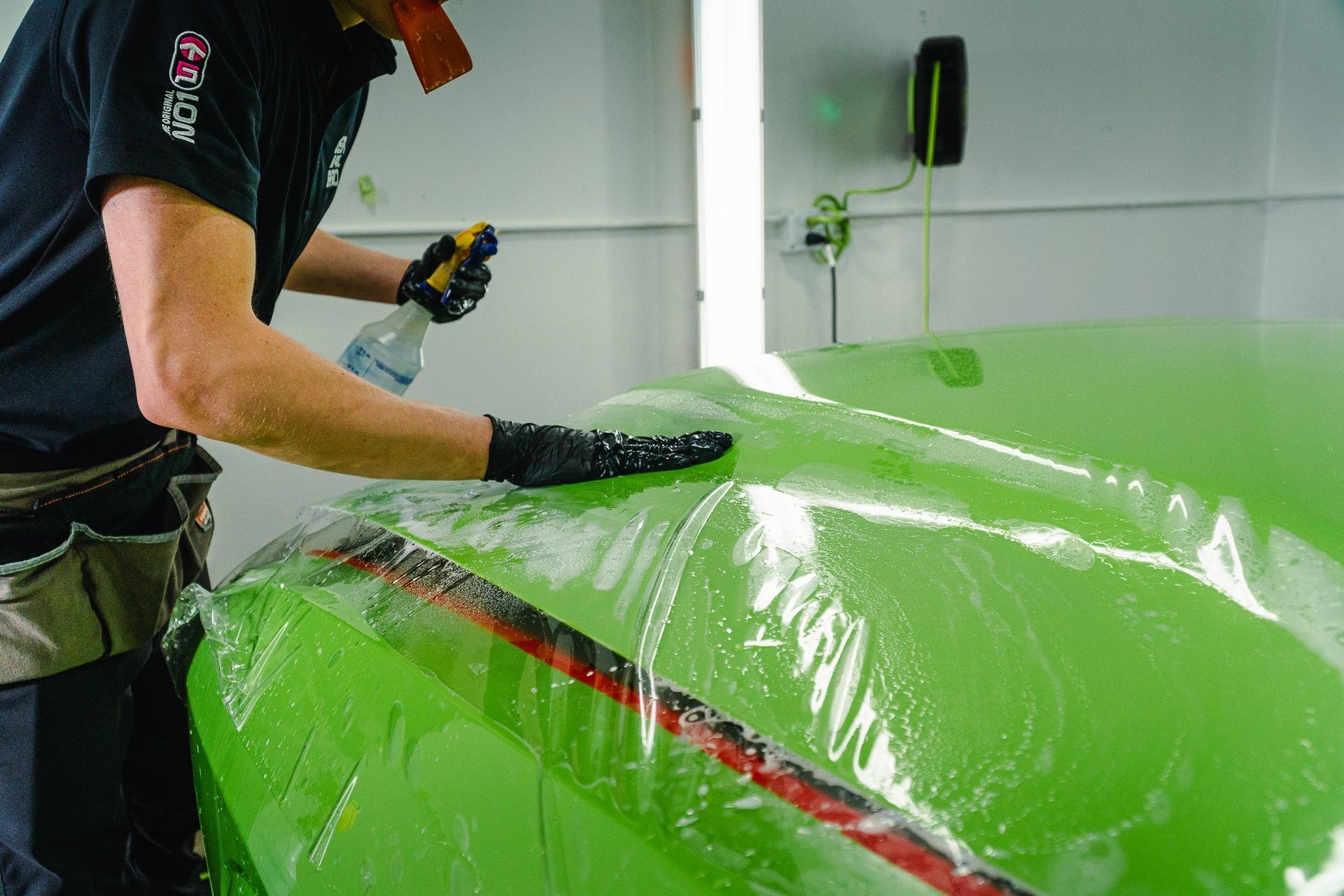 Person applying green paint or coating to a car body in a workshop