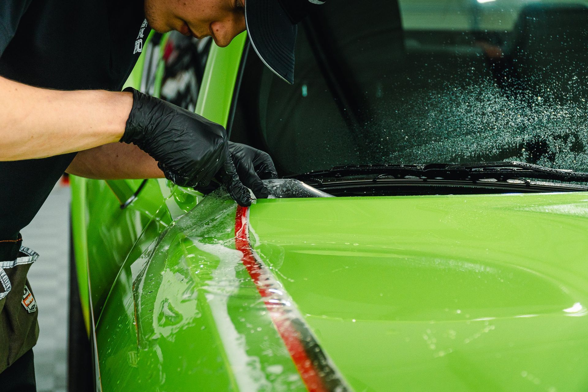 Person applying a red stripe to a bright green car with a heat gun in a workshop