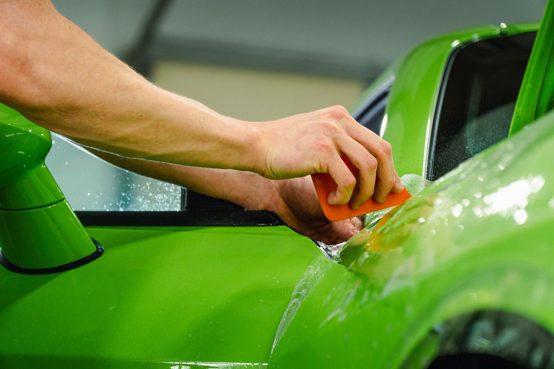 Hand washing a bright green car with a sponge at a car wash