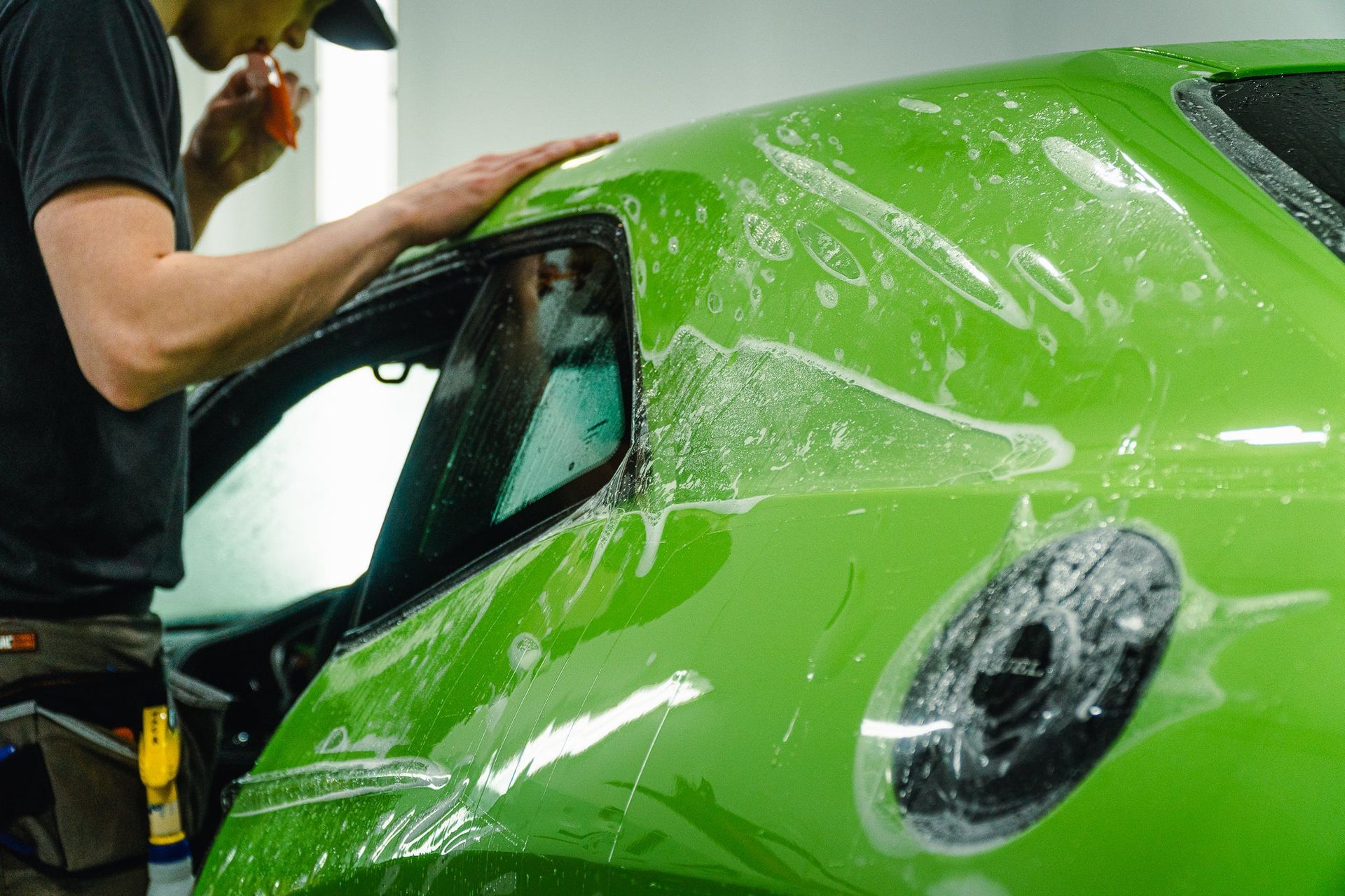 Person polishing a bright green sports car in a workshop