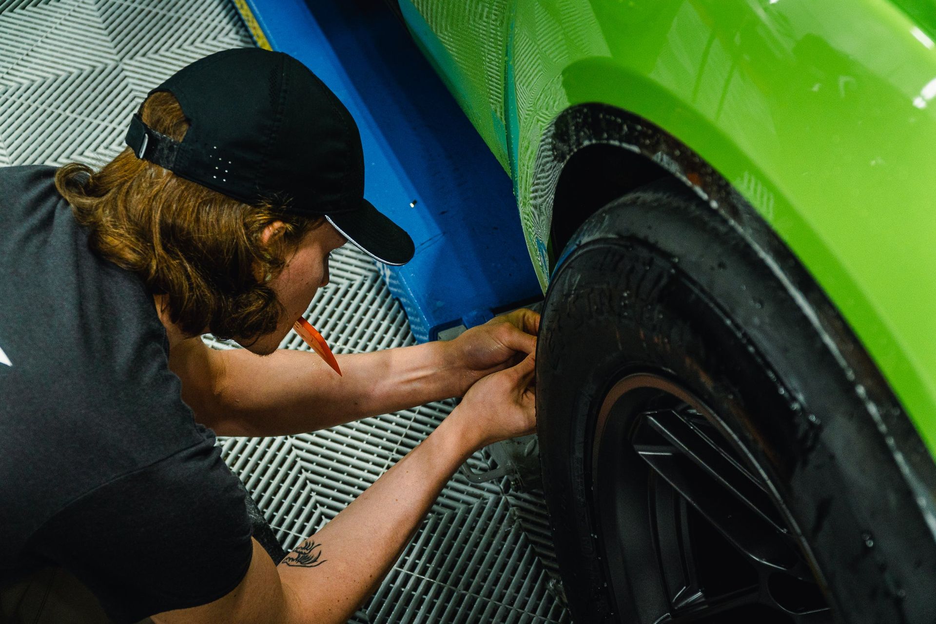 Person polishing a green car’s wheel with a cloth in a garage