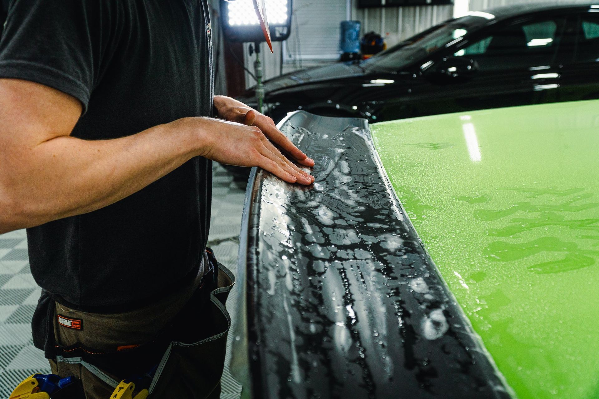 Person smoothing black film on a bright green car hood in a garage