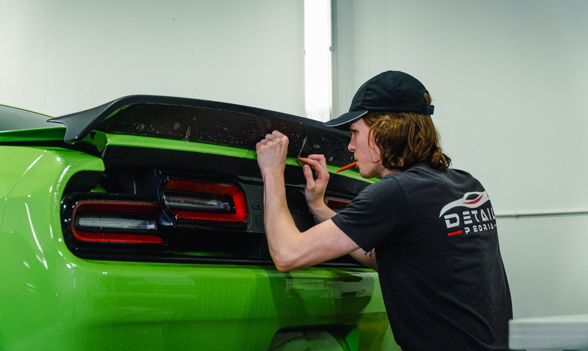 Person applying trim to a bright green car’s rear panel in a garage