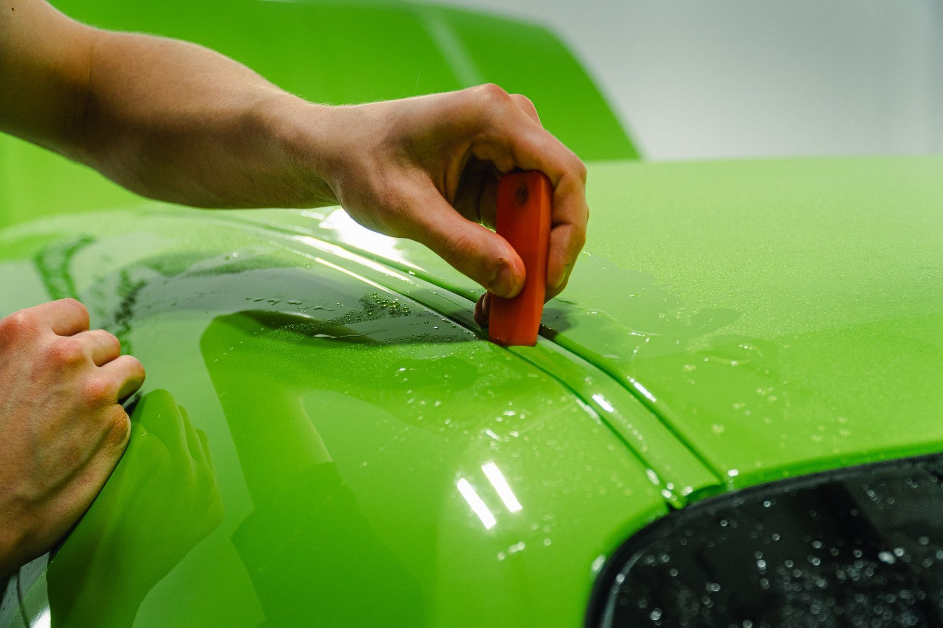 Hands applying orange tape to a bright green car hood